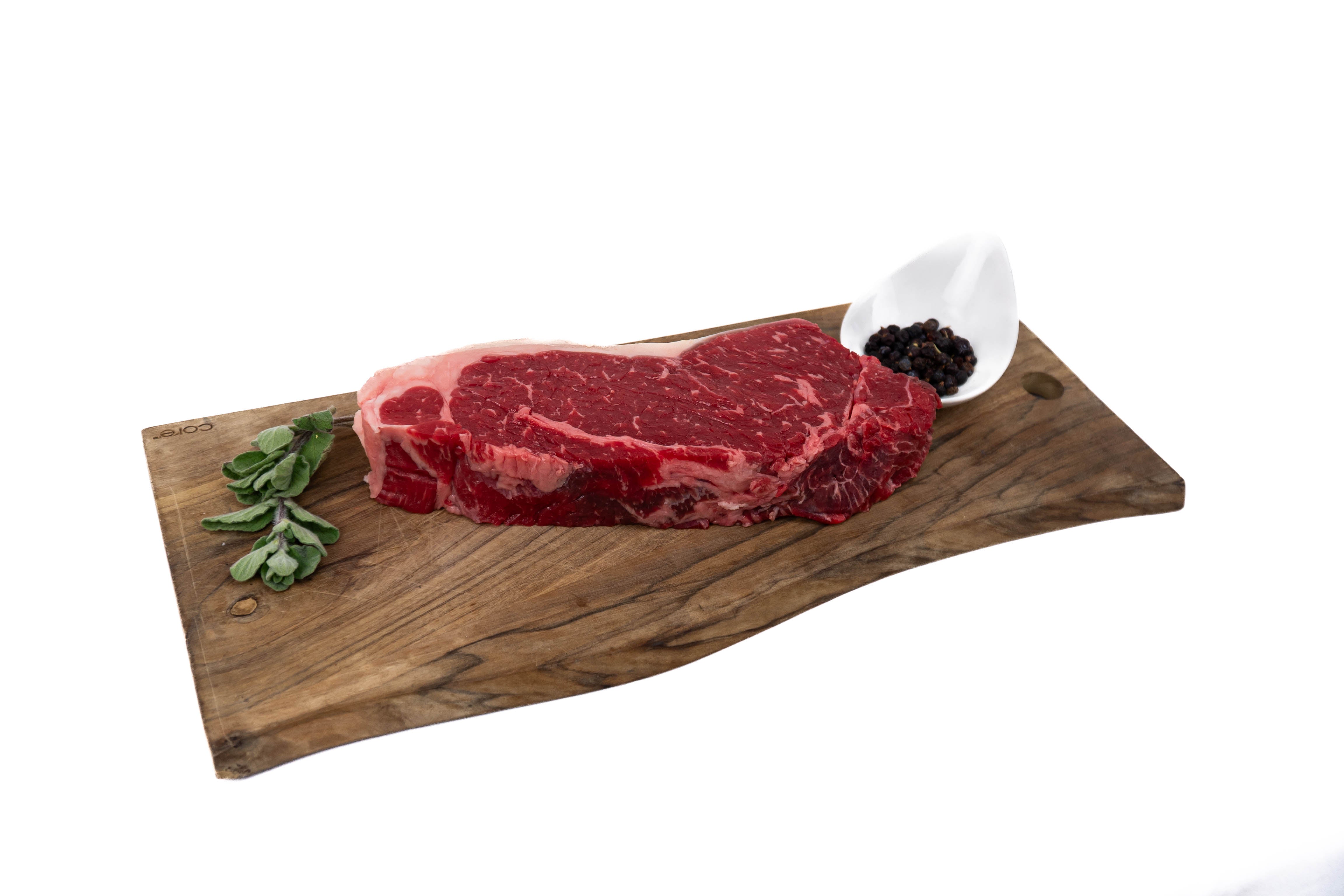 Raw steak on a wooden cutting board with a small bowl of blackberries and a sprig of rosemary.