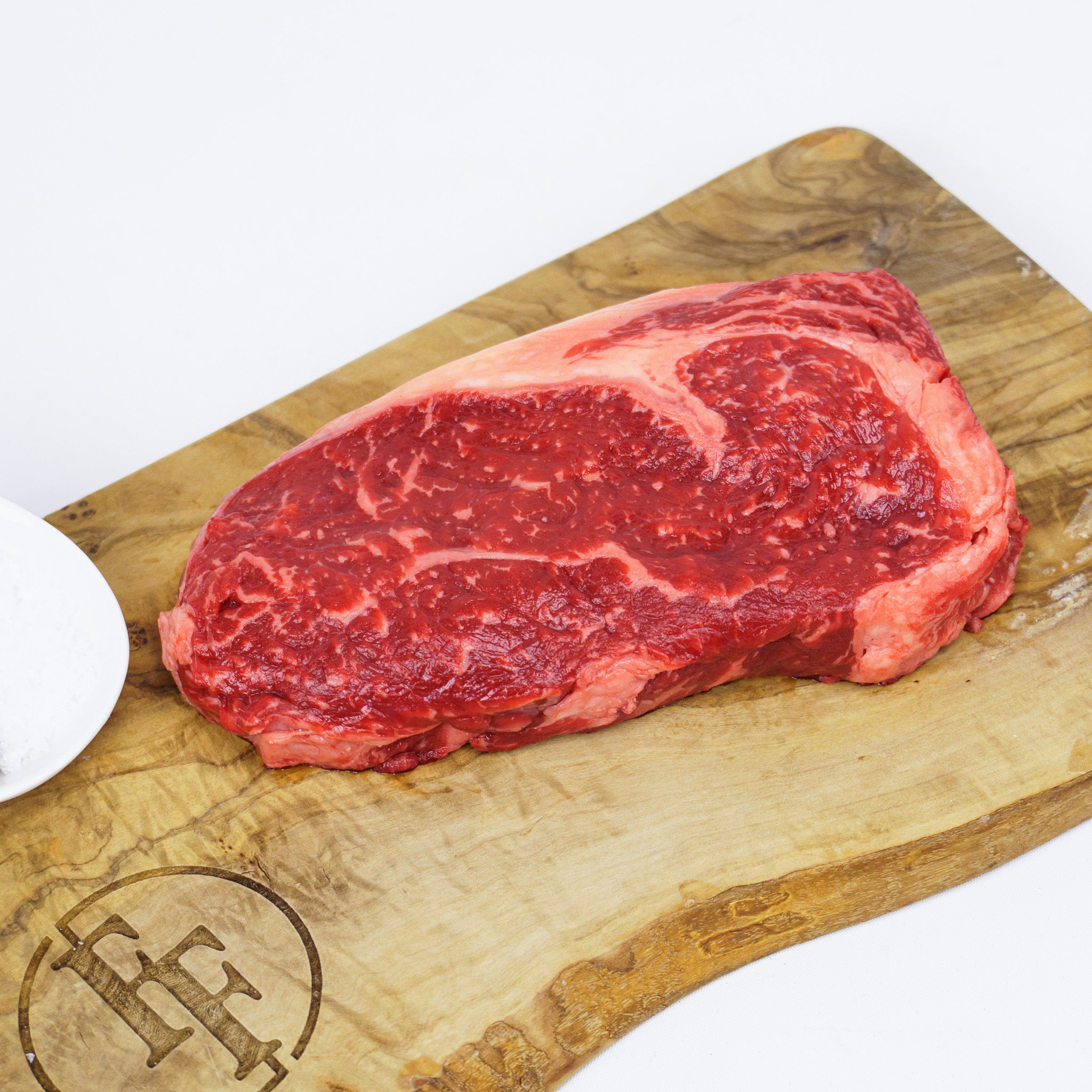 Raw steak on a wooden cutting board with a brand logo.