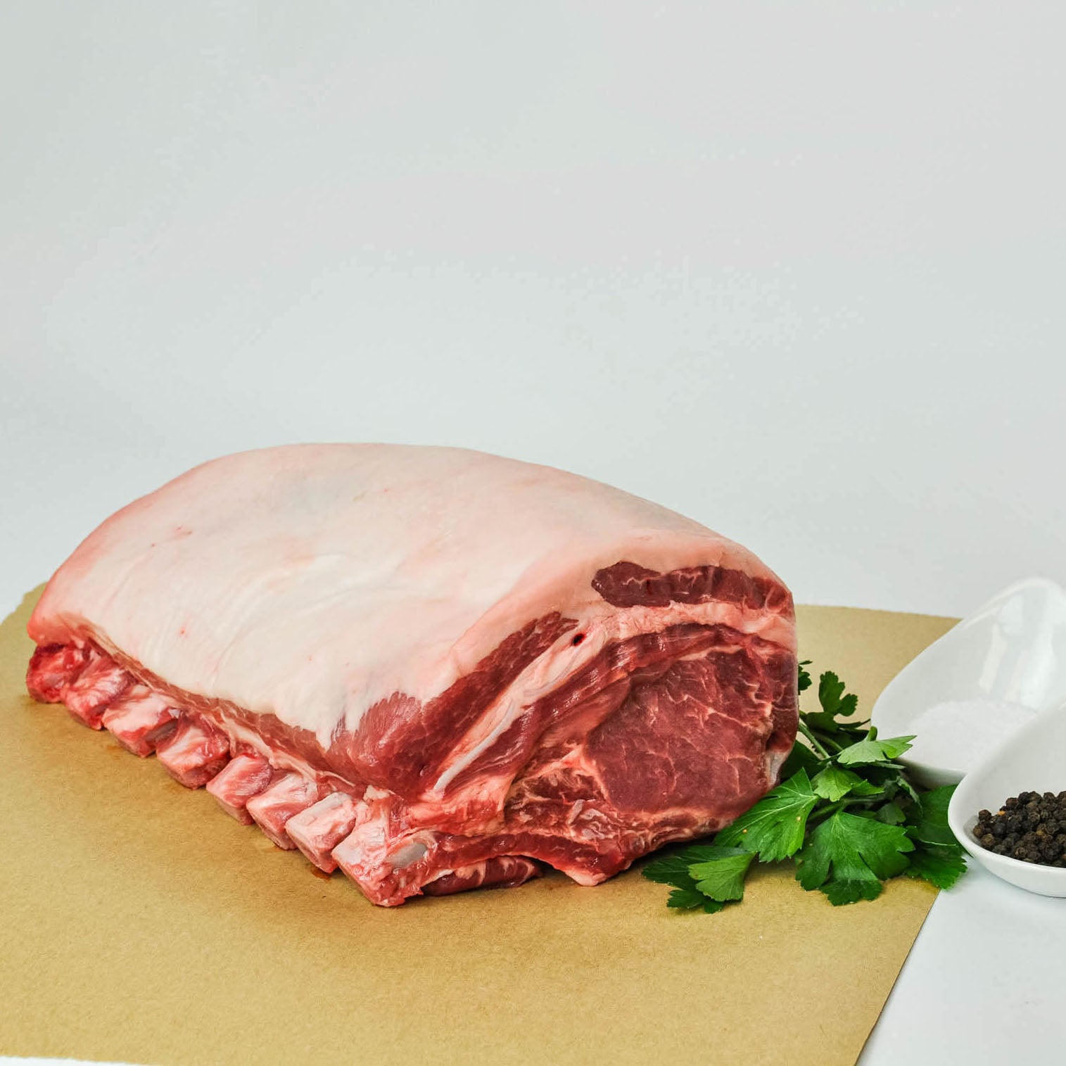 Raw ribeye steak on a cutting board with herbs and spices on a white background