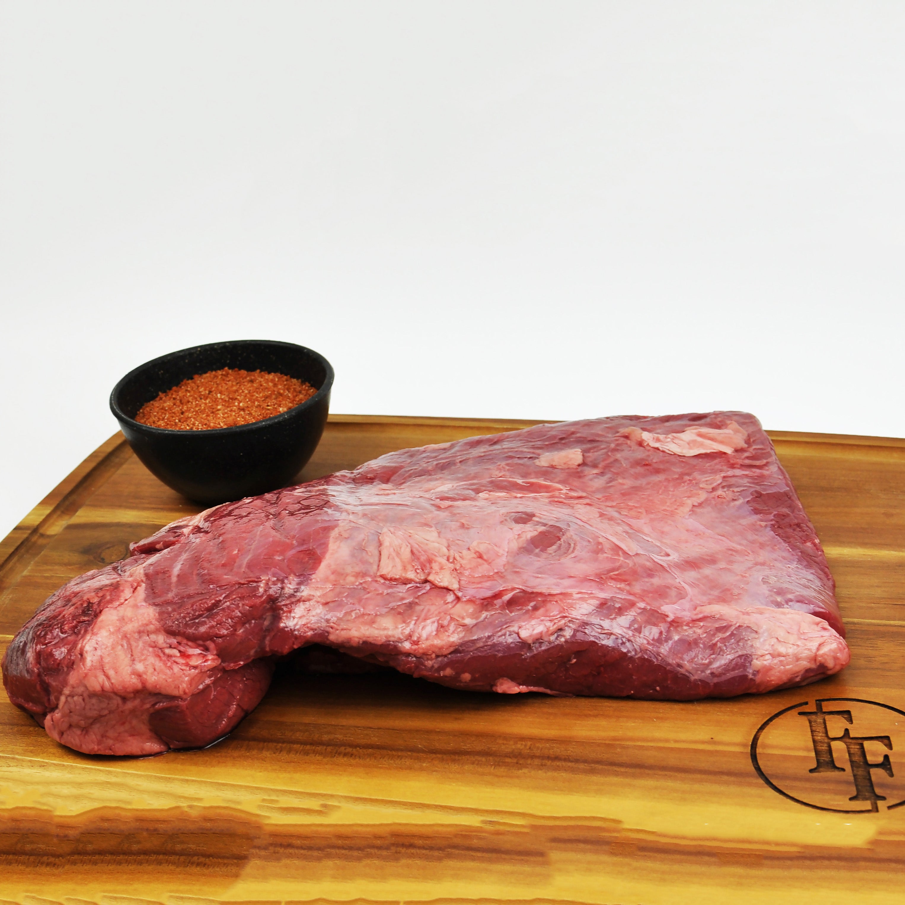 Raw beef brisket on a wooden cutting board with a small bowl of spices.