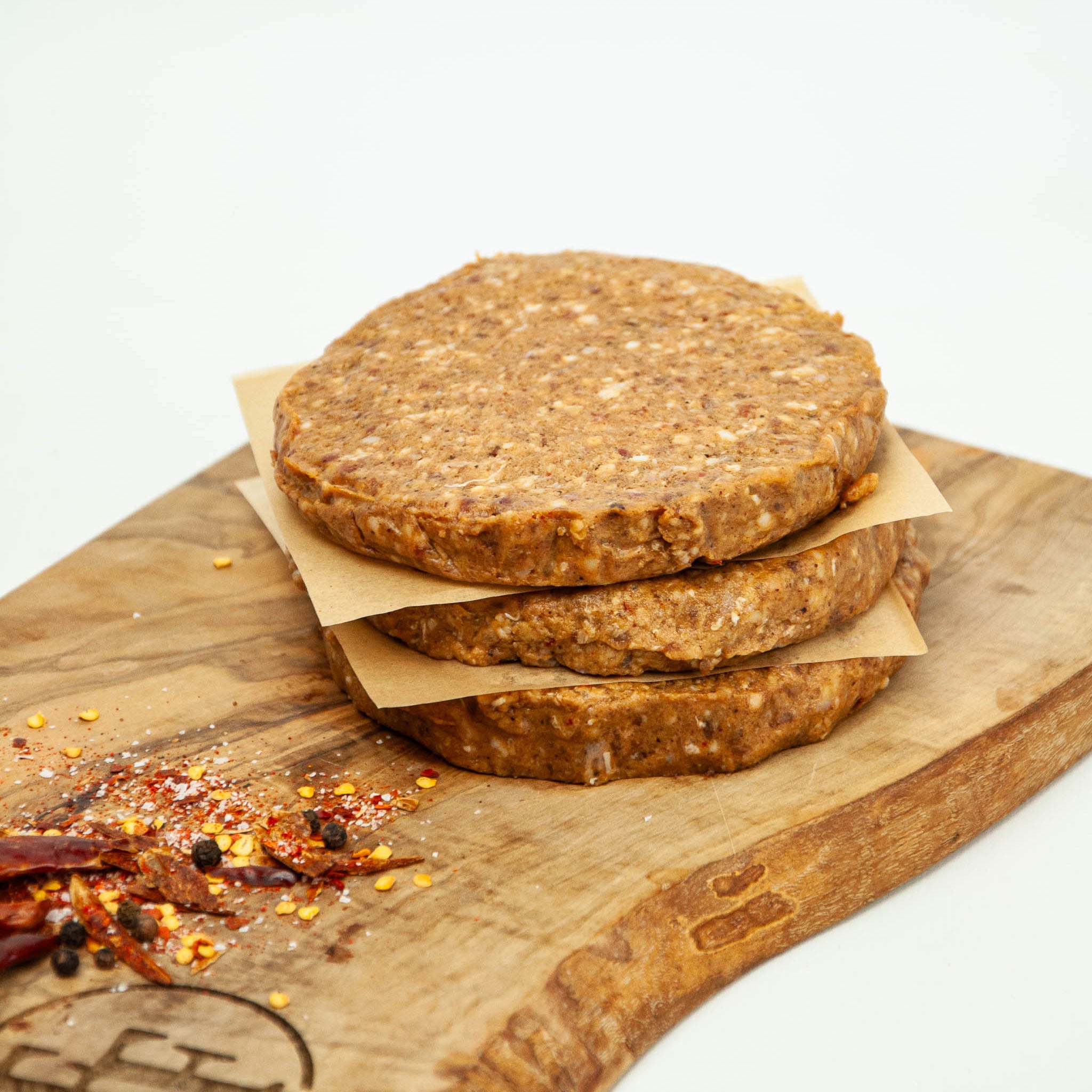 Stack of raw burger patties on a wooden cutting board with spices.
