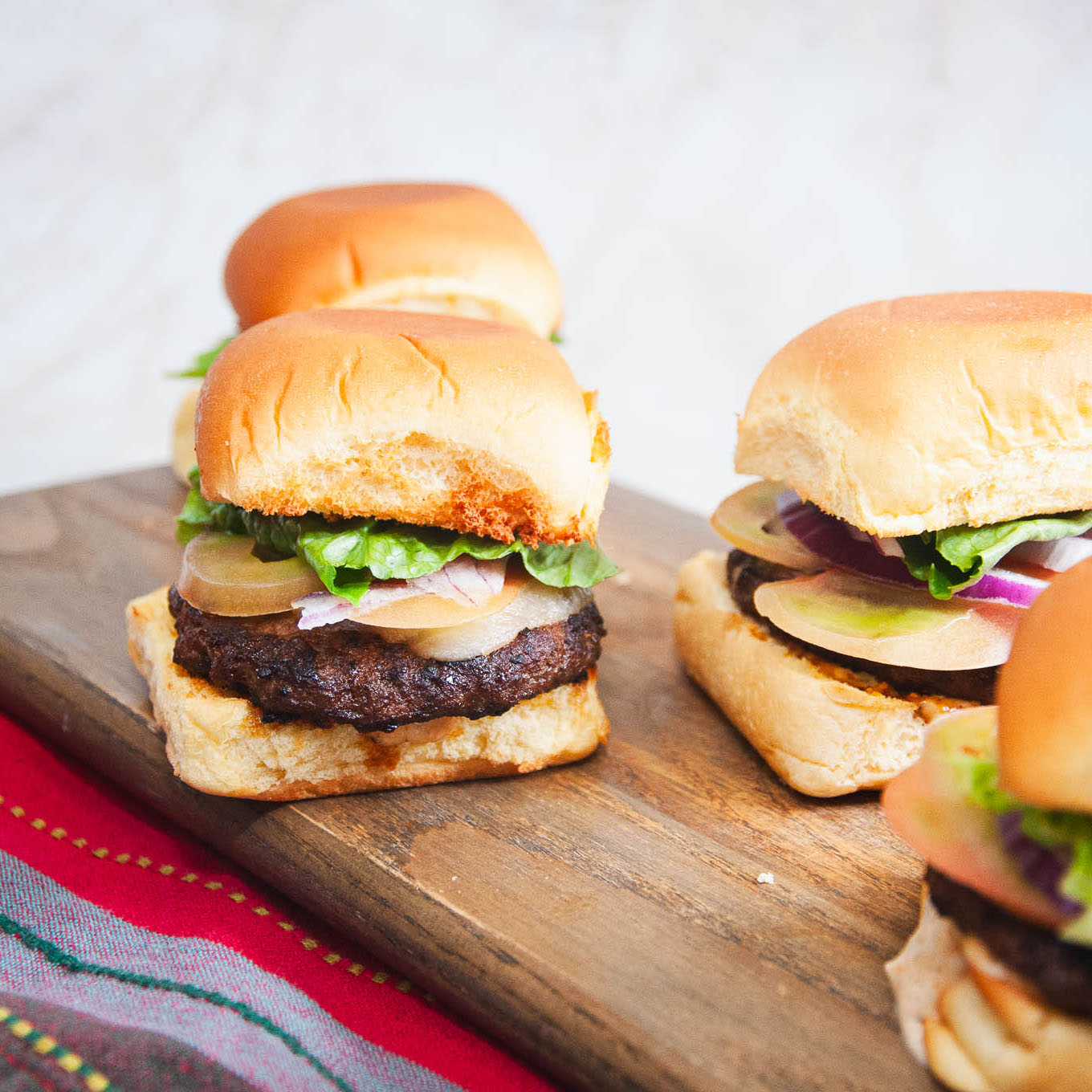 Three sliders with beef patties, lettuce, and onions on a wooden board.