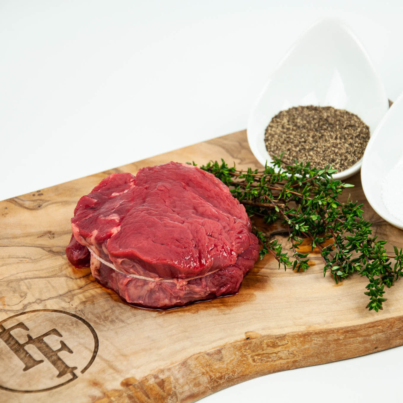 Raw steak on a wooden cutting board with herbs and pepper