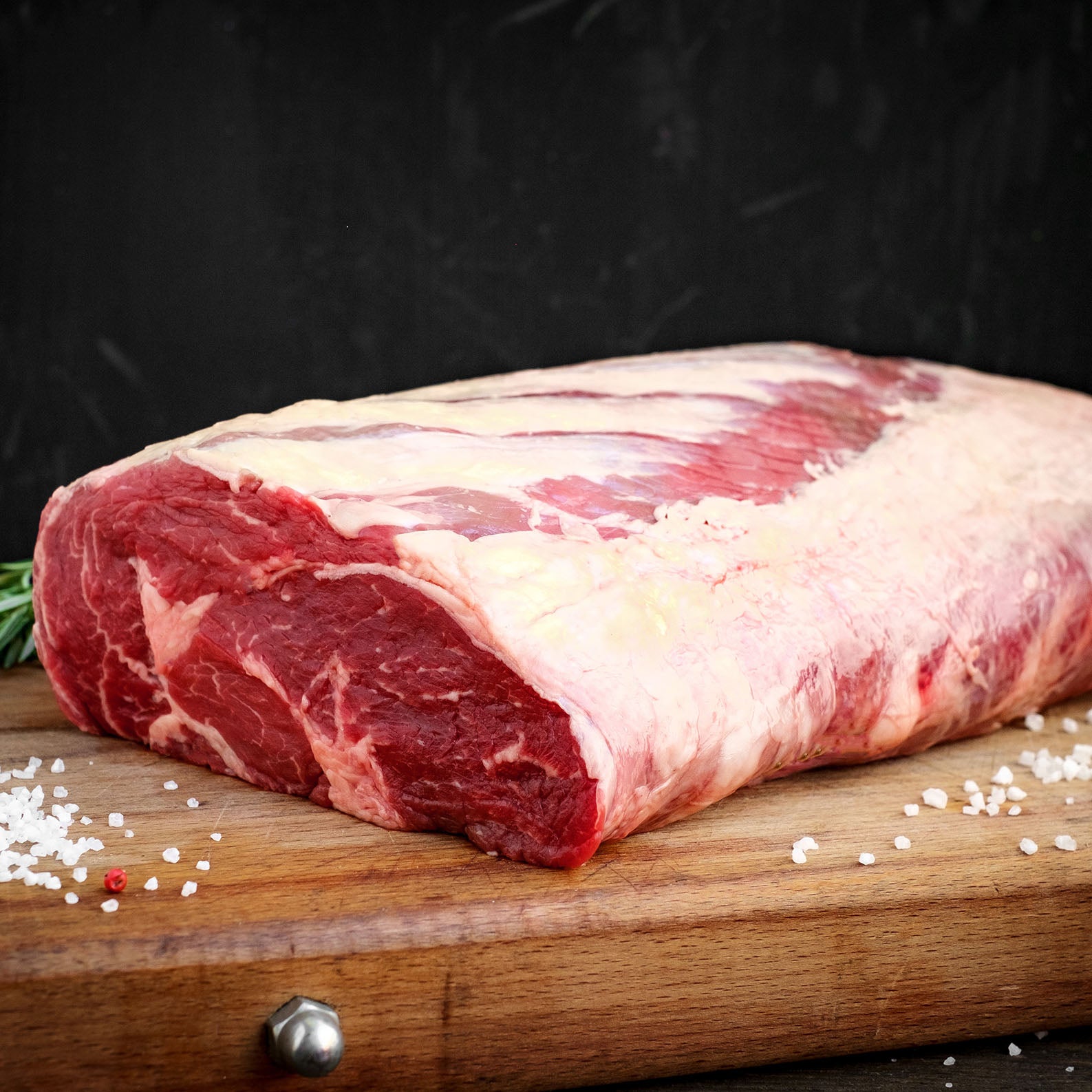 Raw meat on a wooden cutting board with spices and rosemary