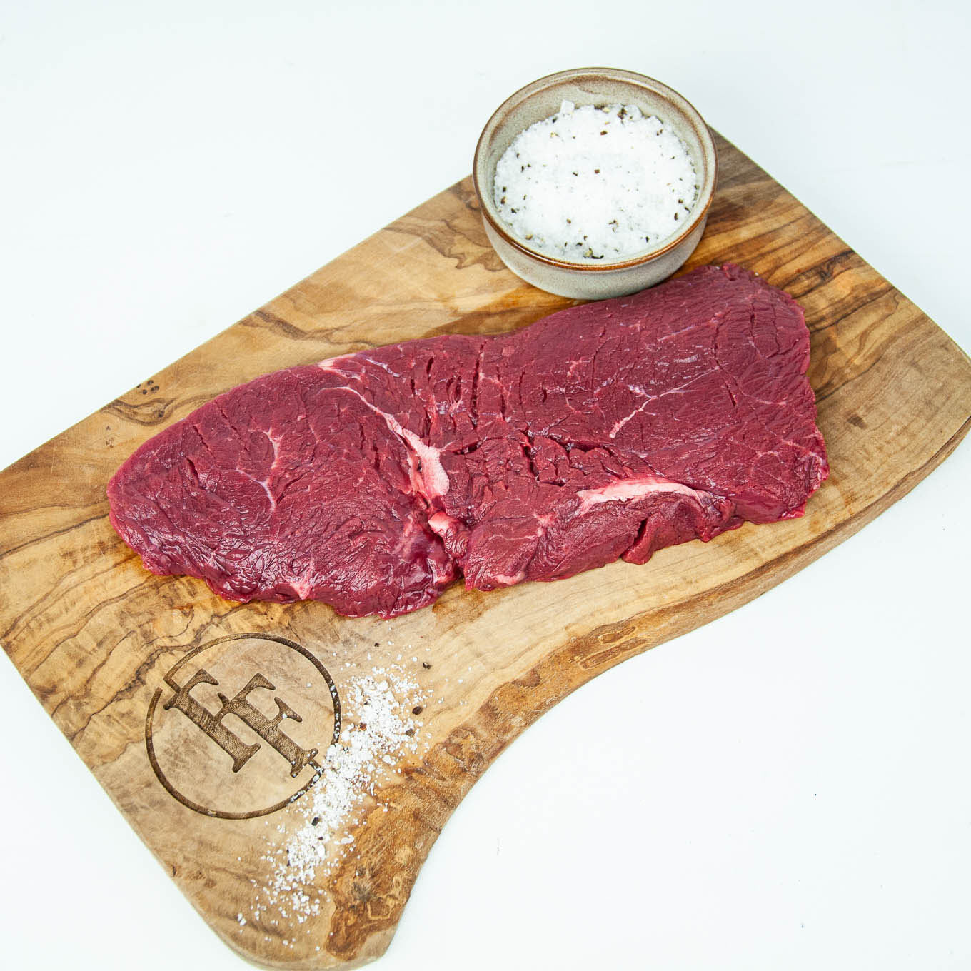 Two raw steaks on a wooden cutting board with a salt container, branded 'FF'.