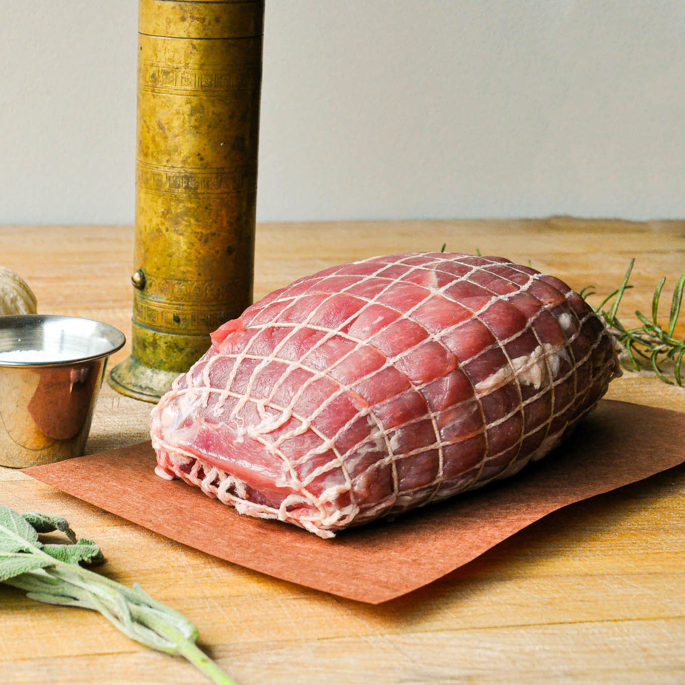 Raw meat on a wooden cutting board with herbs and a pepper grinder.