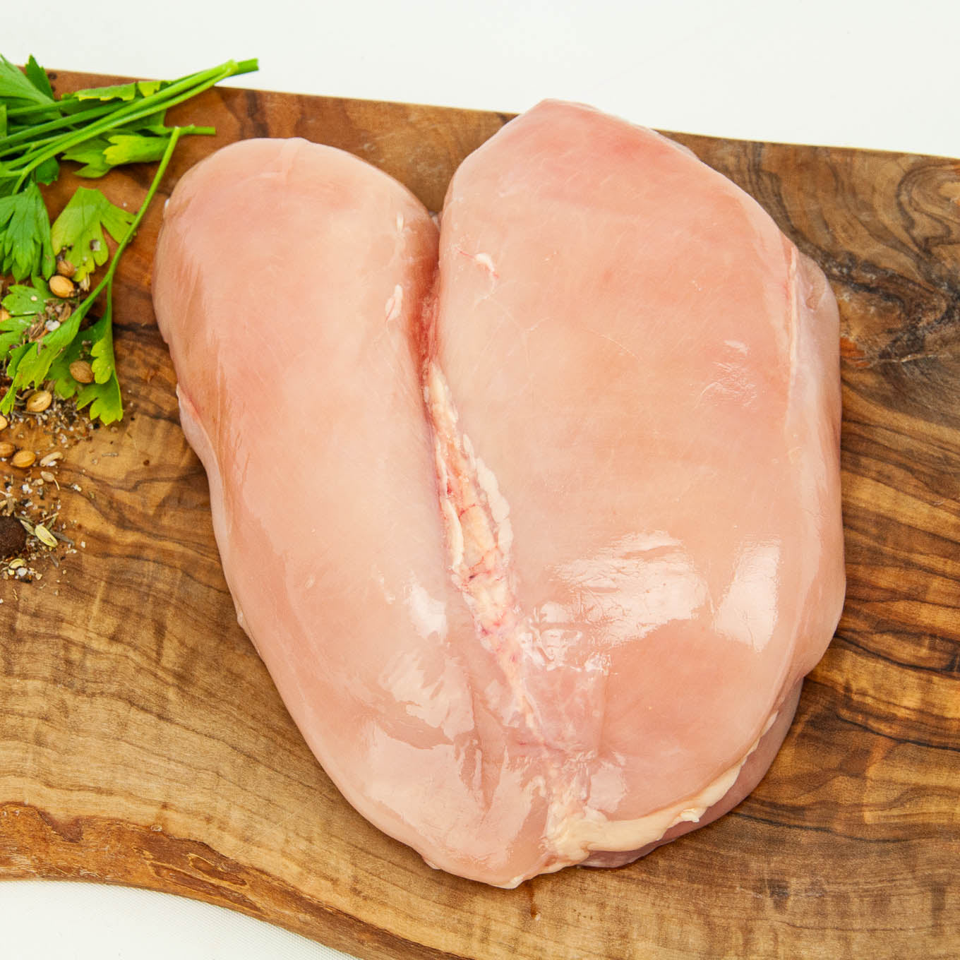 Raw chicken breast on a wooden cutting board with herbs and spices.
