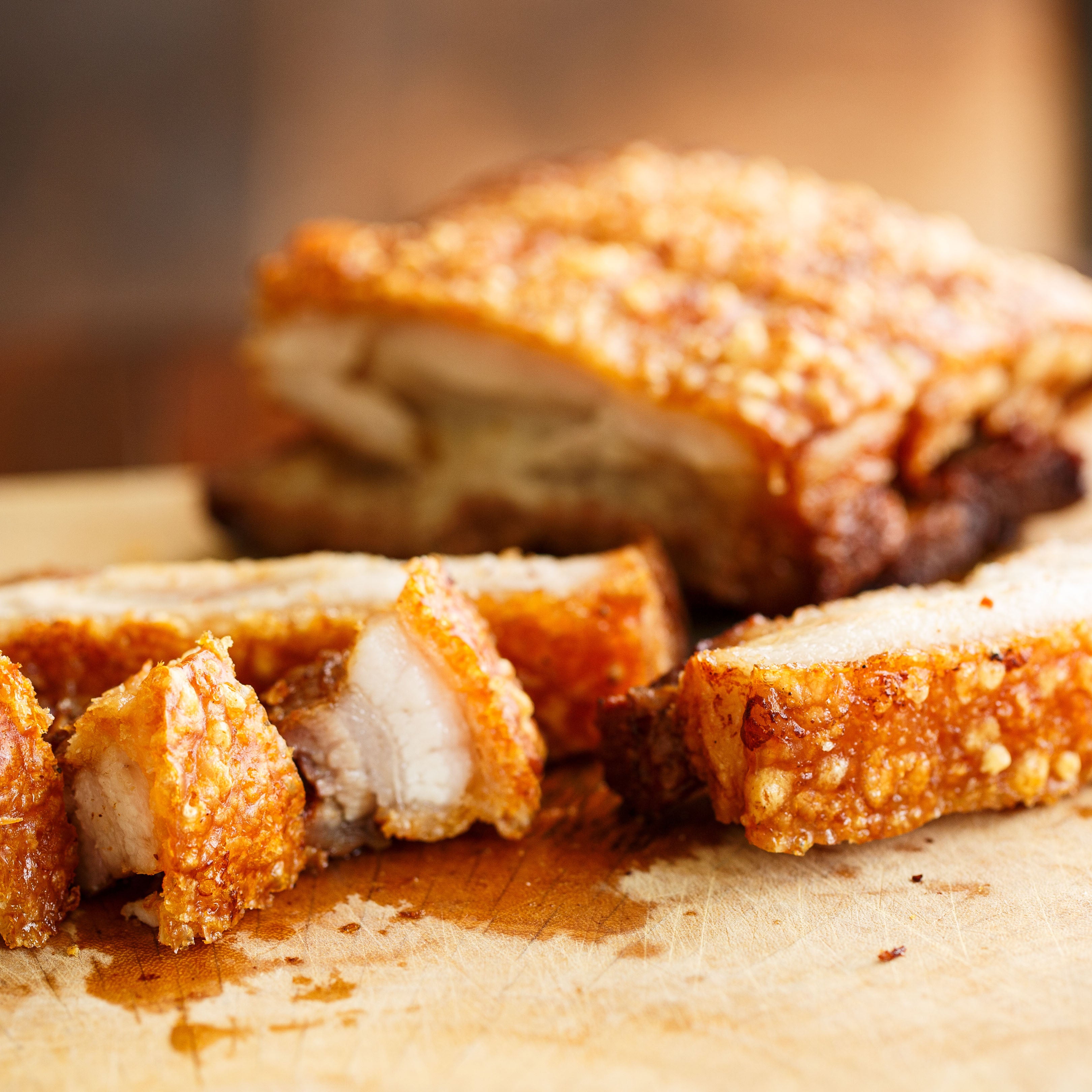Sliced roasted pork belly on a wooden cutting board with a blurred background