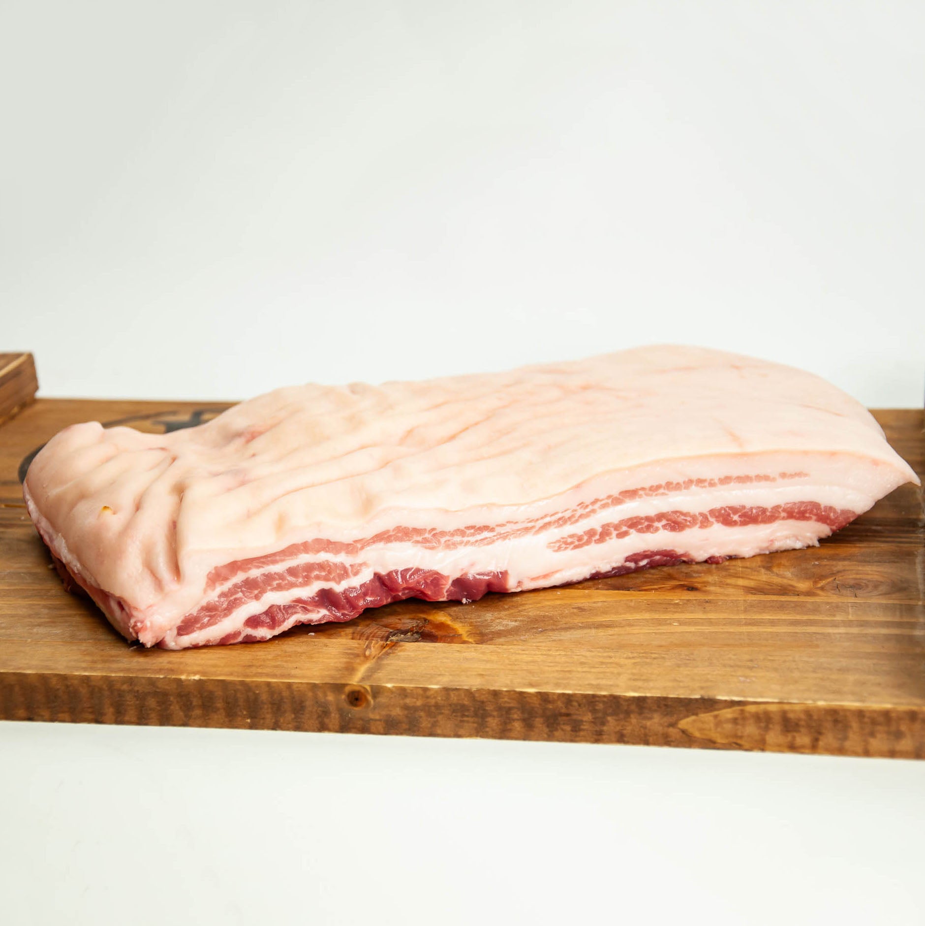 Raw pork belly on a wooden cutting board with a white background