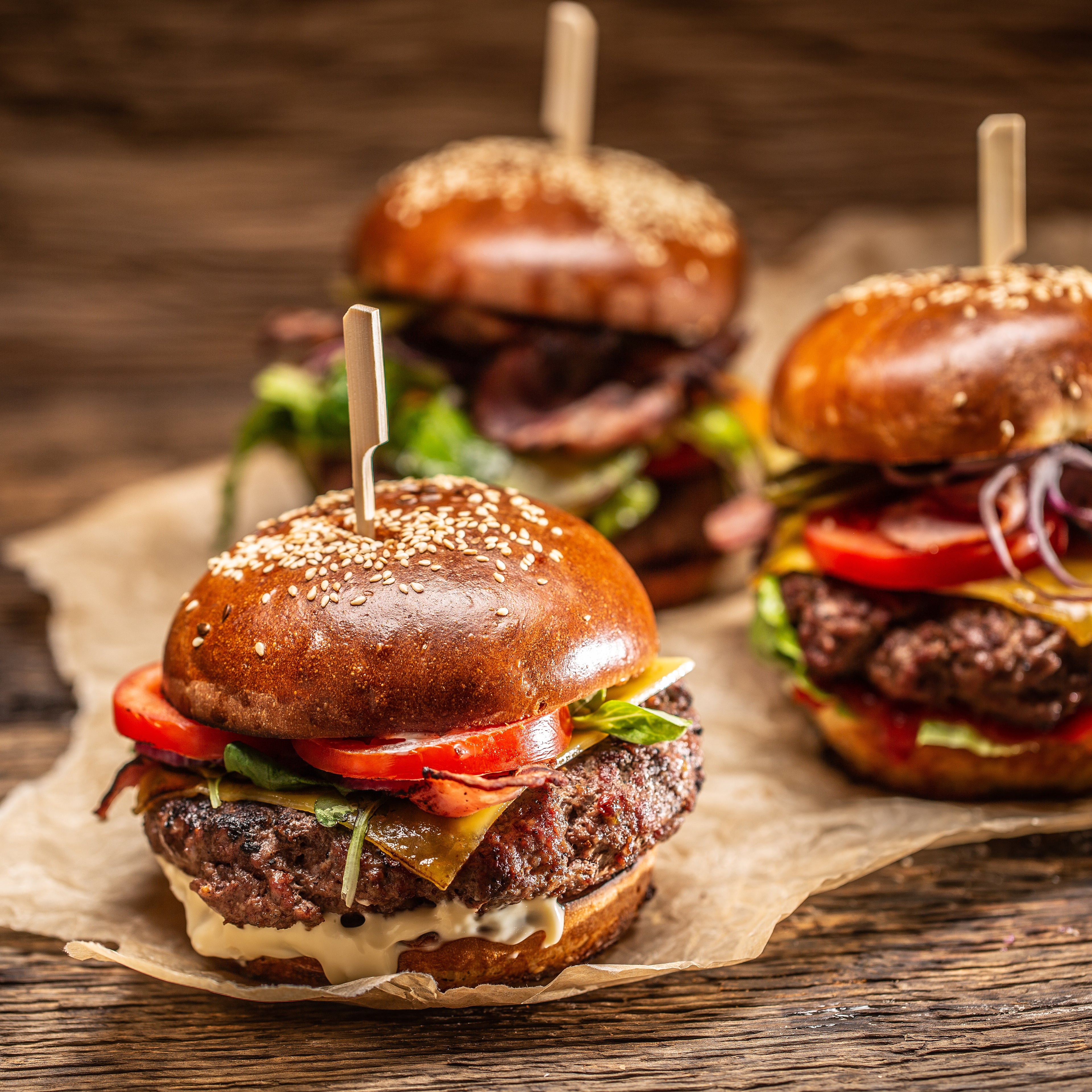 Three delicious-looking burgers on a wooden surface with a rustic background