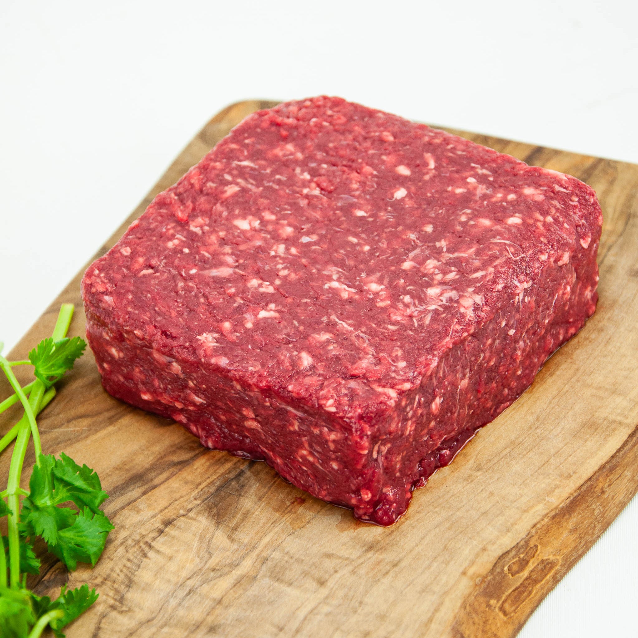 Block of raw ground beef on a wooden cutting board with fresh herbs.