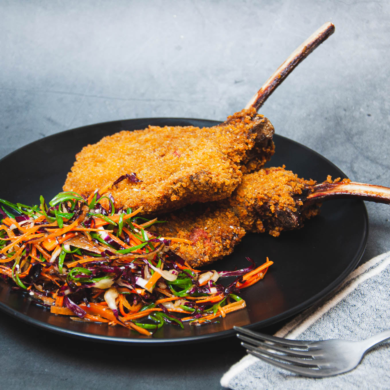 Fried lamb chops with a side of colorful salad on a black plate.