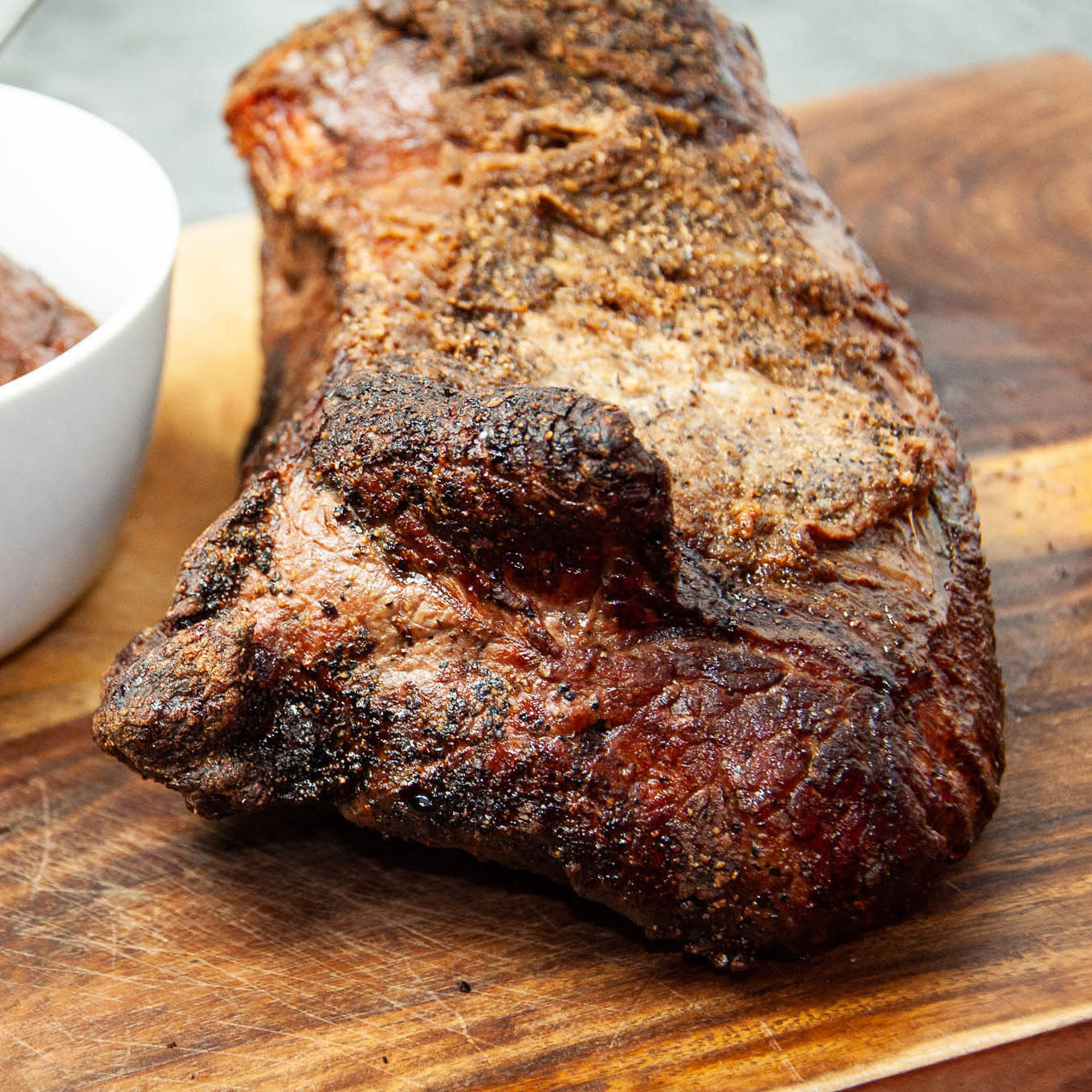 Roasted beef on a wooden cutting board with a side of sauce.