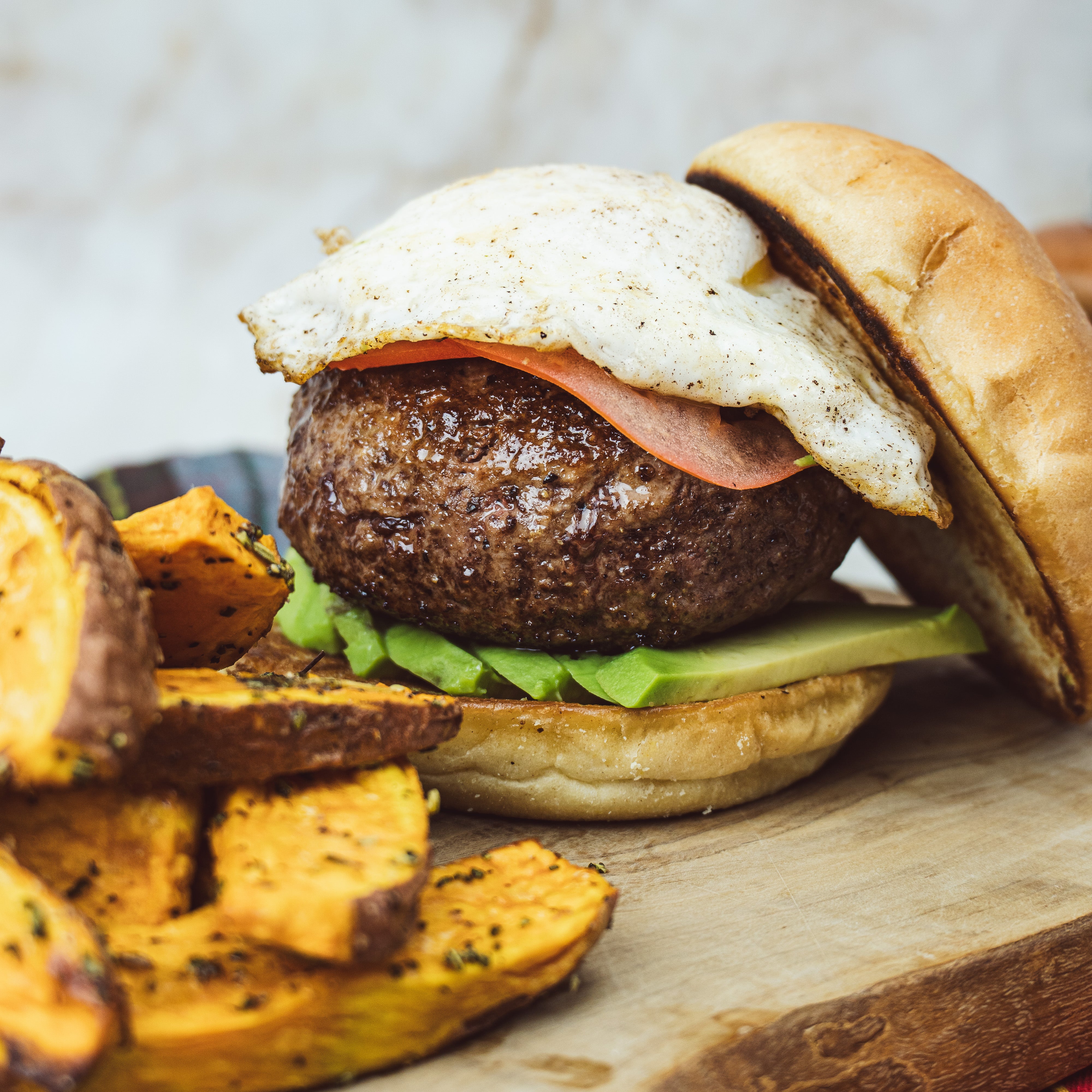 a photo of a cooked burger with sweet potato fries and avacado