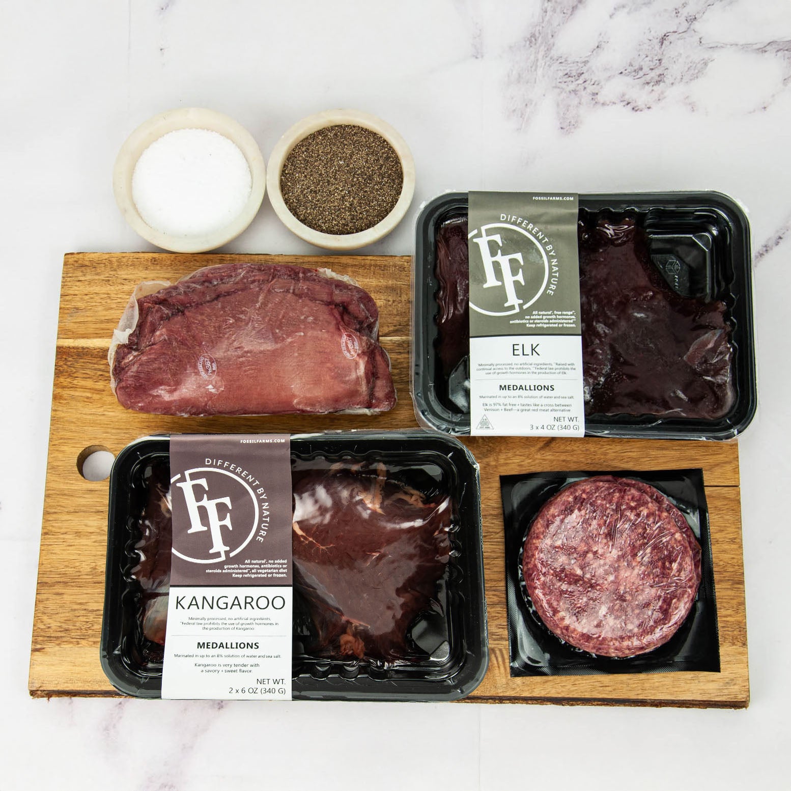 Assorted packaged meats including elk and kangaroo on a wooden cutting board with salt and pepper.