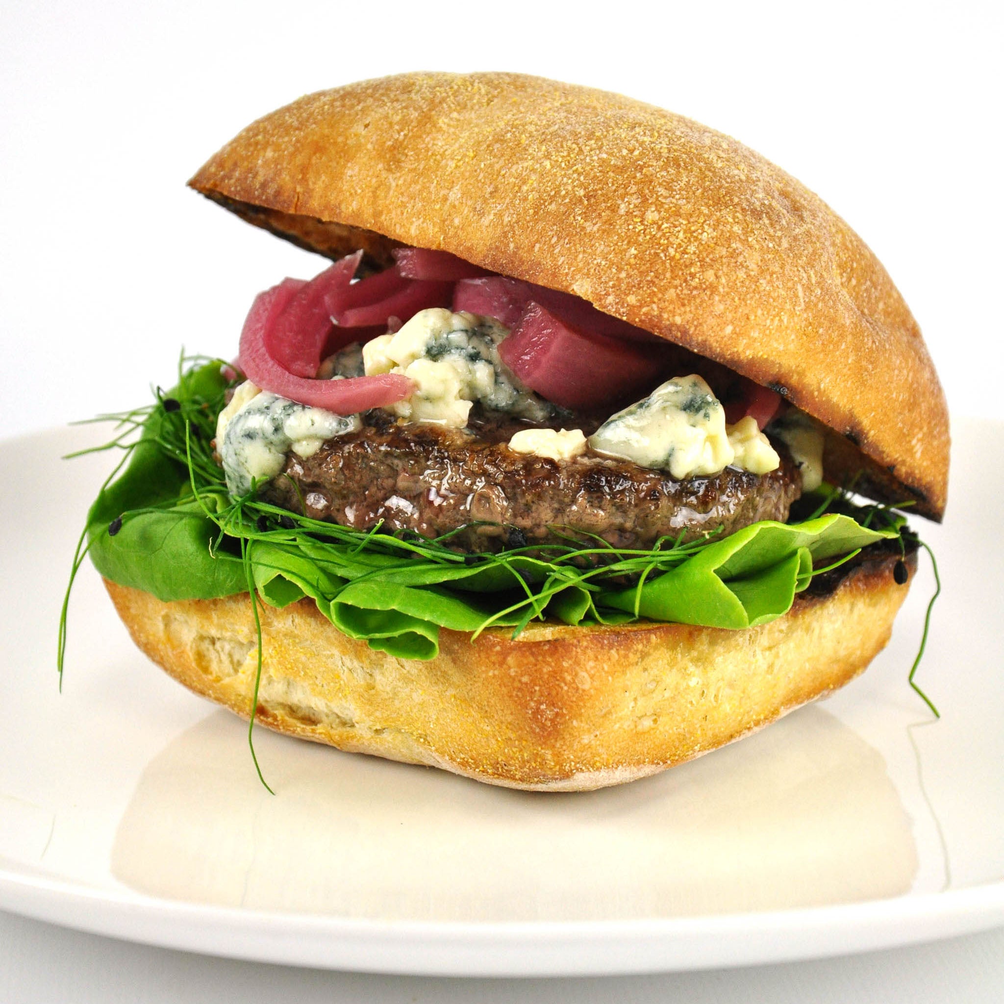 Delicious burger with lettuce, blue cheese, and pickled onions on a white plate.