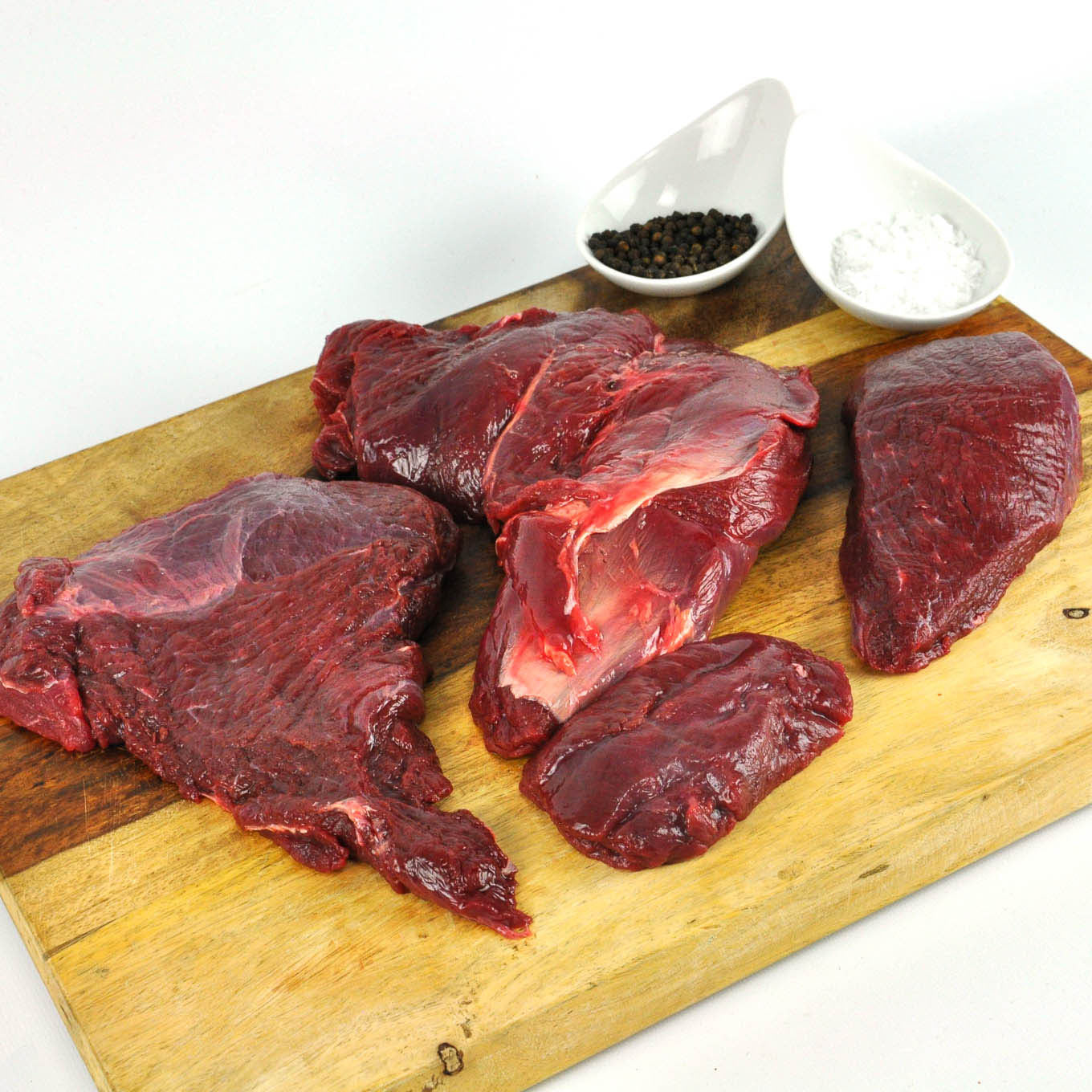 Raw beef on a wooden cutting board with salt and pepper shakers.