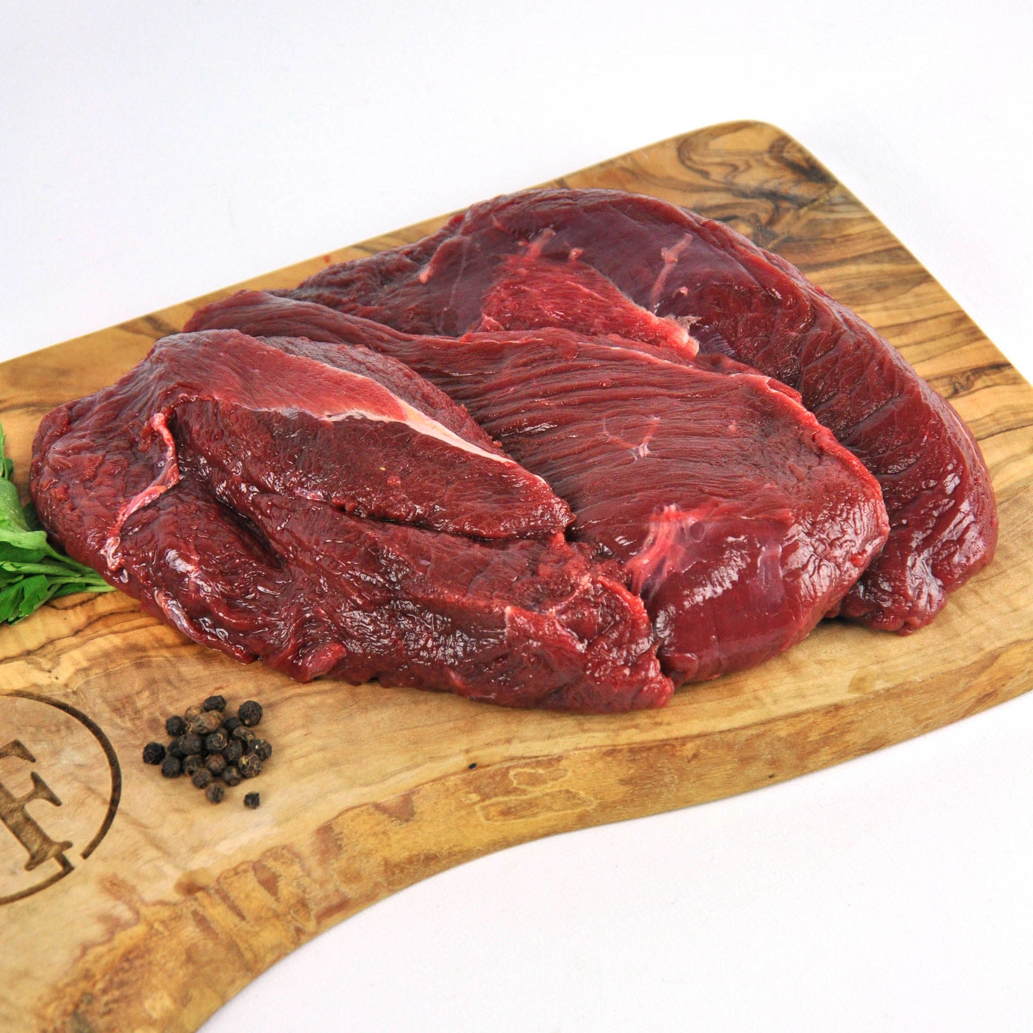 Raw beef on a wooden cutting board with peppercorns and a brand logo.