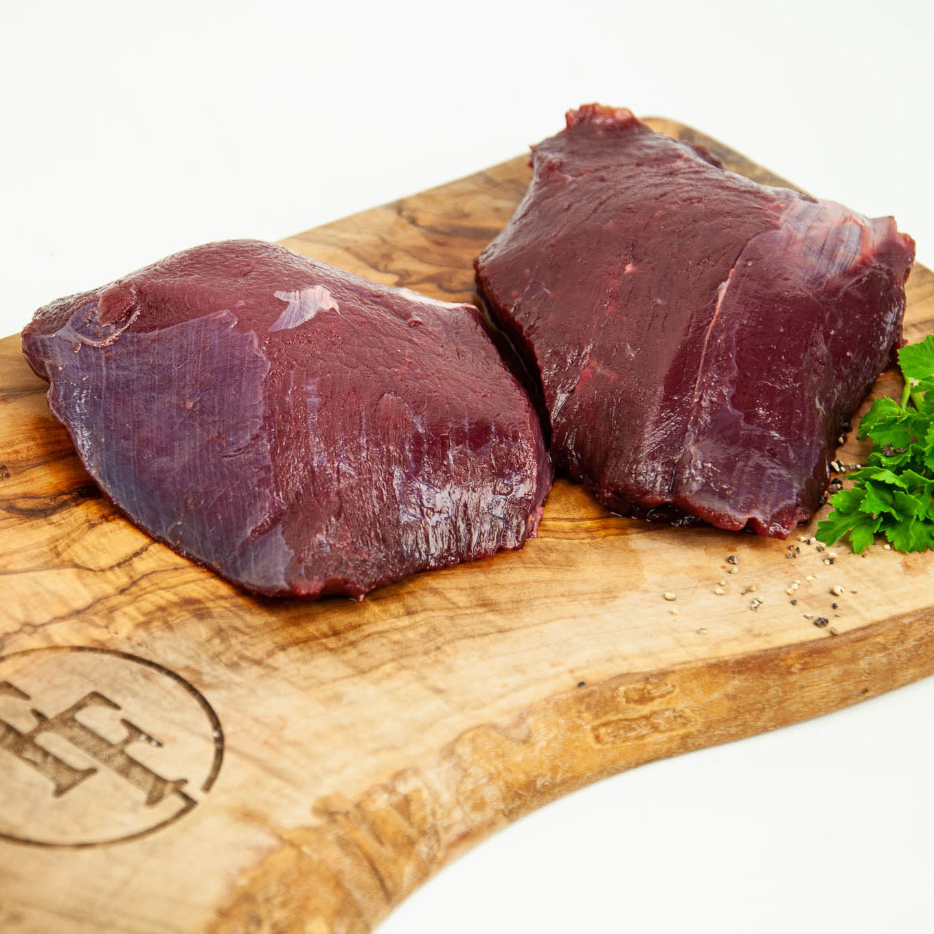 Two pieces of raw kanagroo on a wooden cutting board with a brand logo.