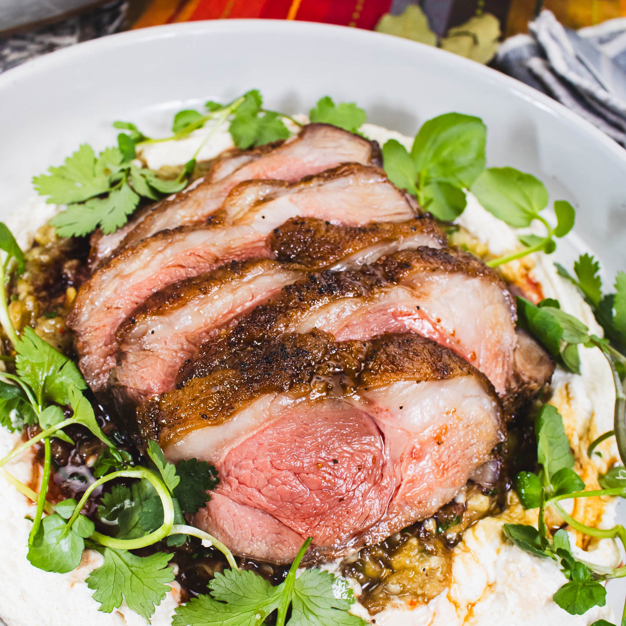Sliced roasted beef with green herbs on a white plate