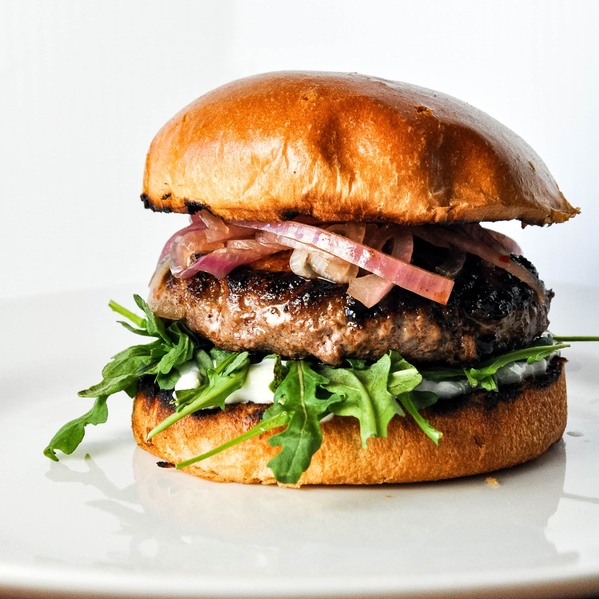 Hamburger with arugula and sliced onions on a white plate