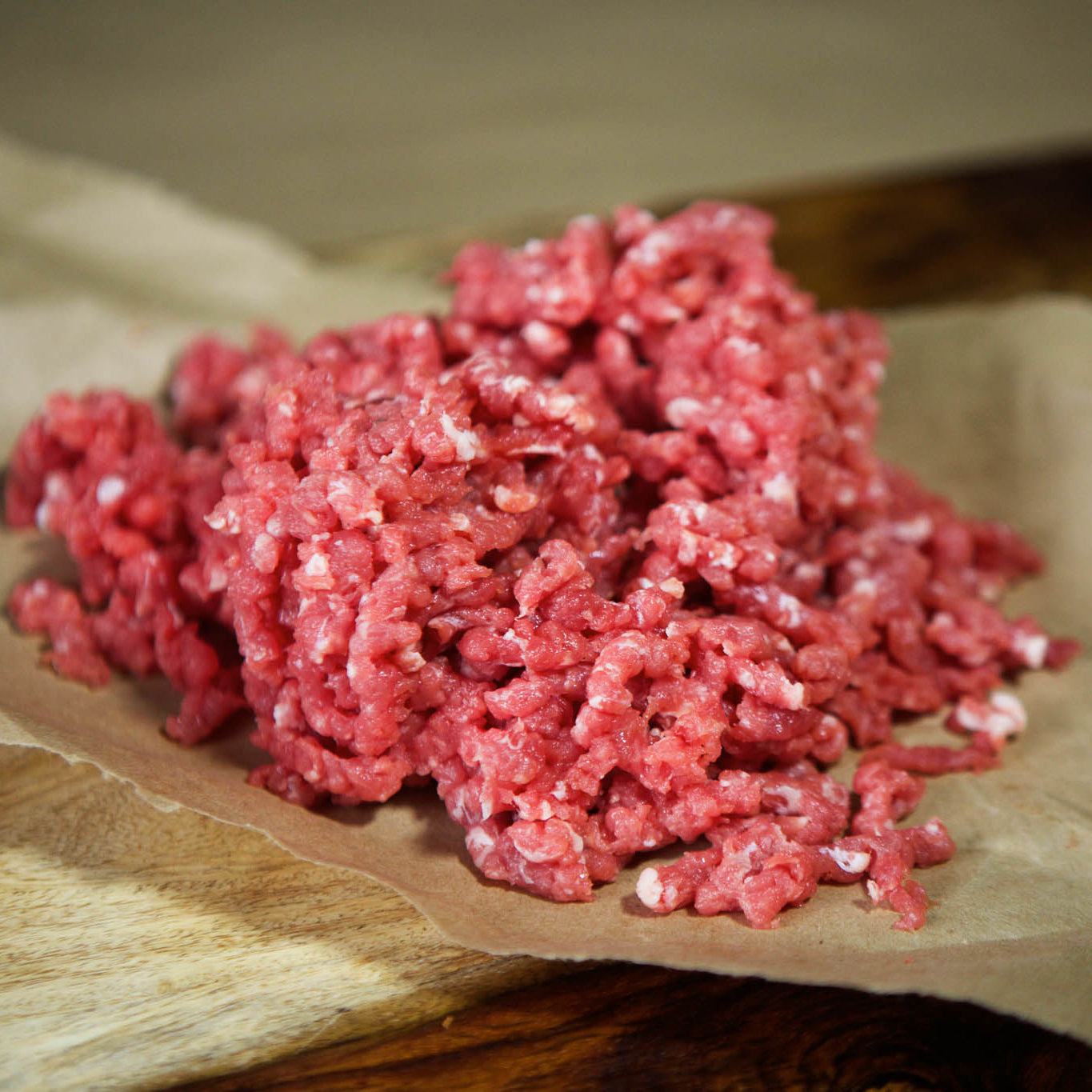 Raw ground meat on a wooden cutting board with brown paper underneath