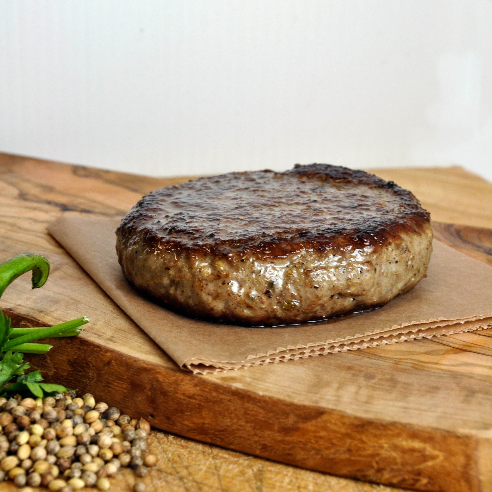 Grilled hamburger patty on a wooden cutting board with herbs and spices.