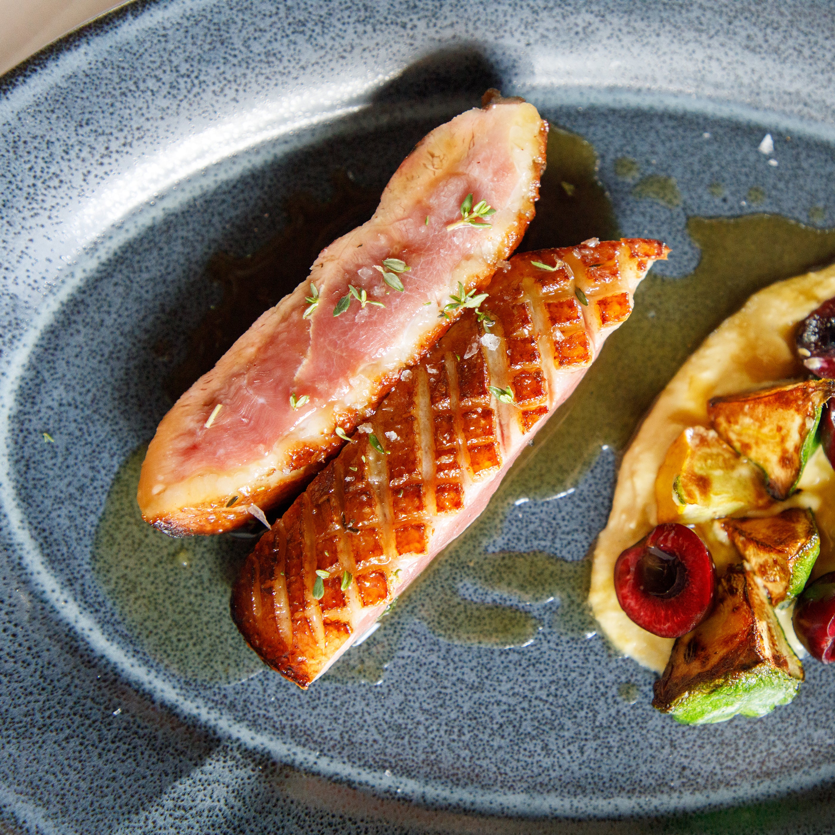 Sliced cooked meat with a side of vegetables on a gray plate