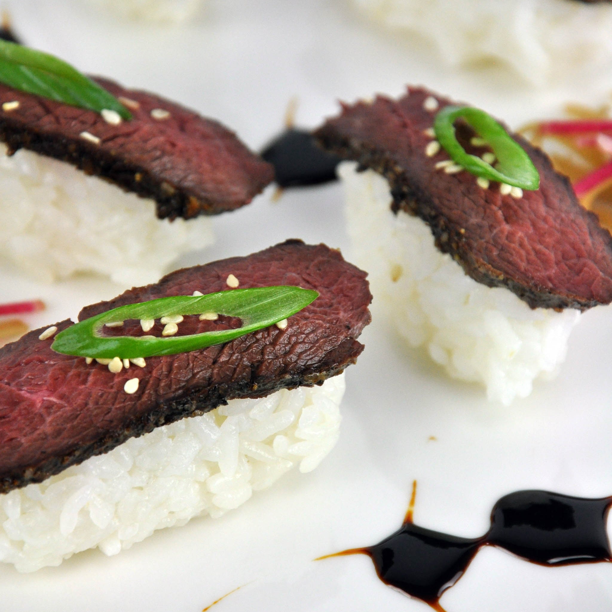 Sushi rolls with beef and green onions on a plate with soy sauce.