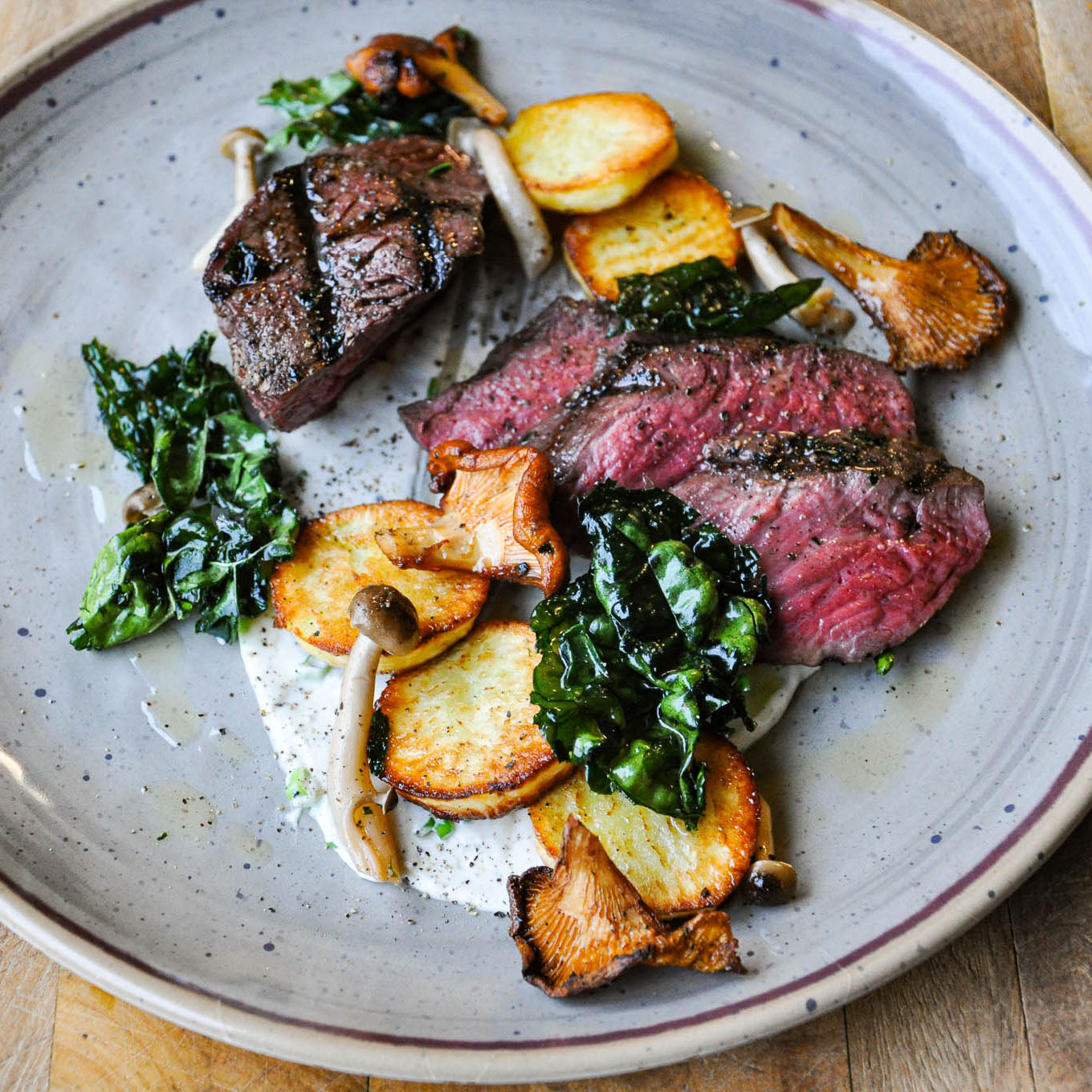 Plated dish of sliced steak with greens and mushrooms on a rustic plate.