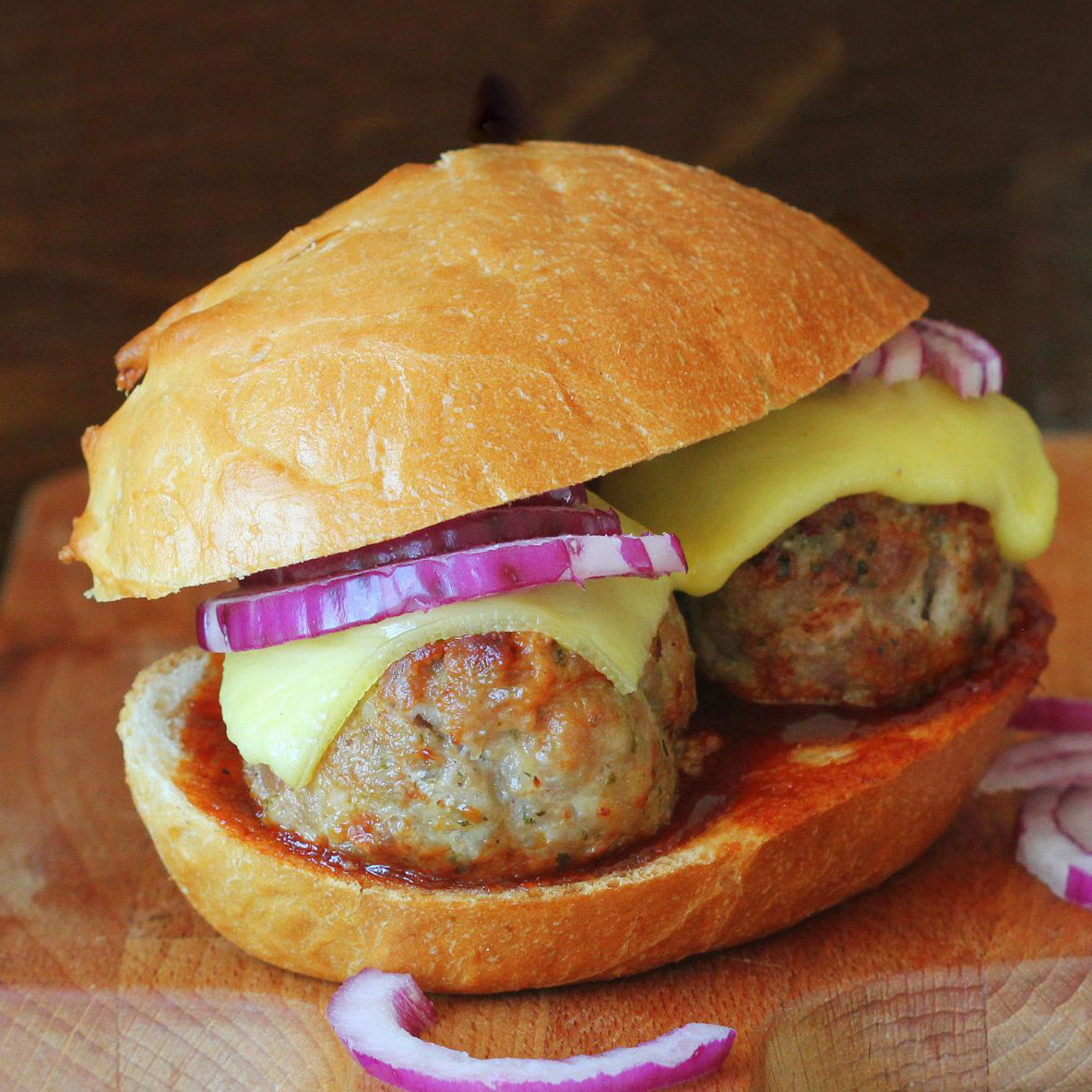 Hamburger with meat patty, cheese, and red onion on a wooden cutting board.