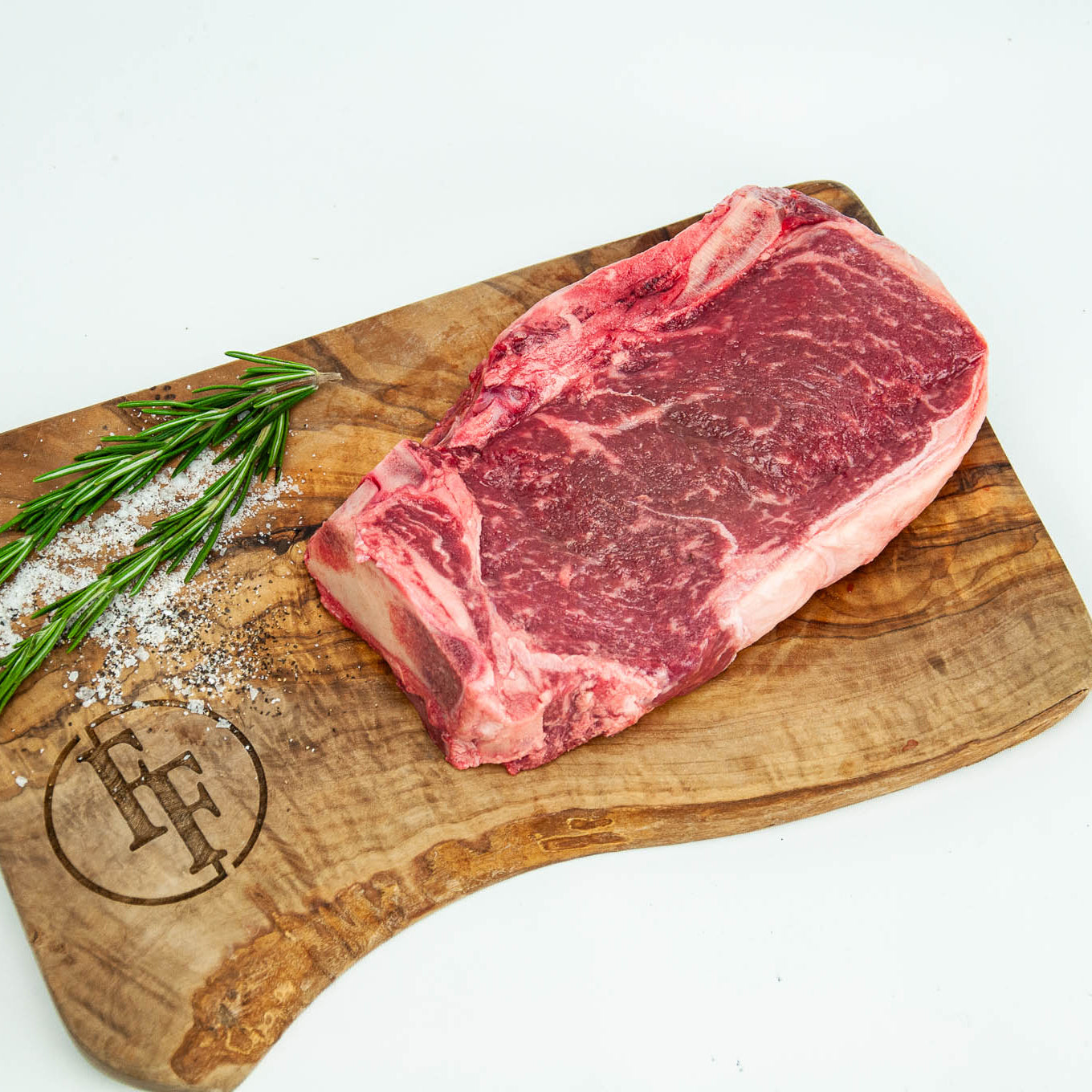Raw steak on a wooden cutting board with rosemary and salt, branded 'FF'.