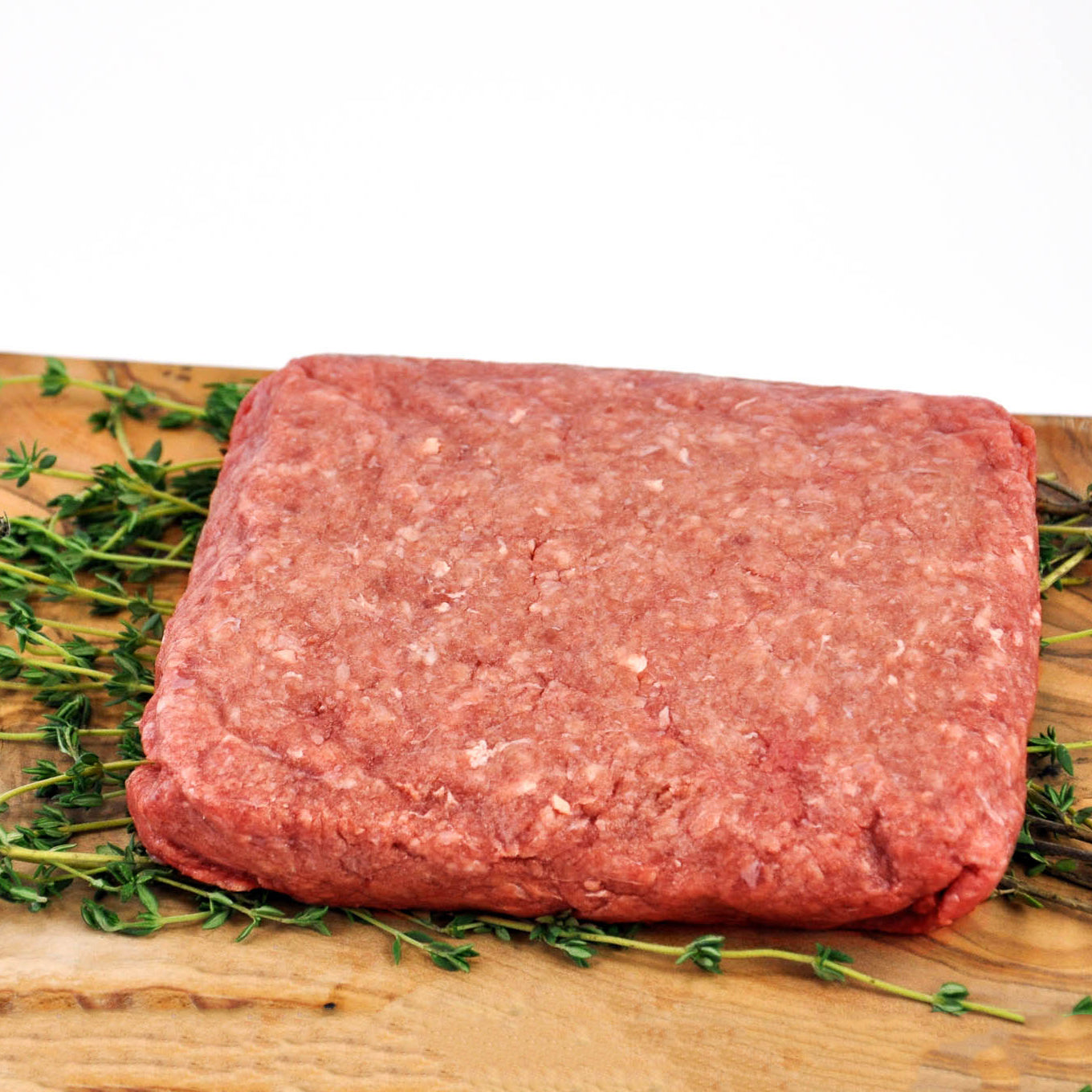 Raw ground meat on a wooden cutting board with fresh herbs