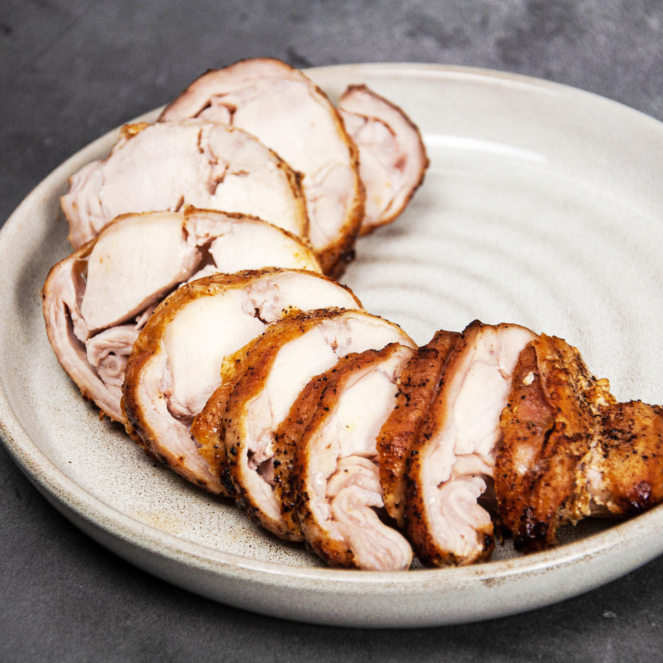 Sliced roasted rabbit on a white plate with a dark background