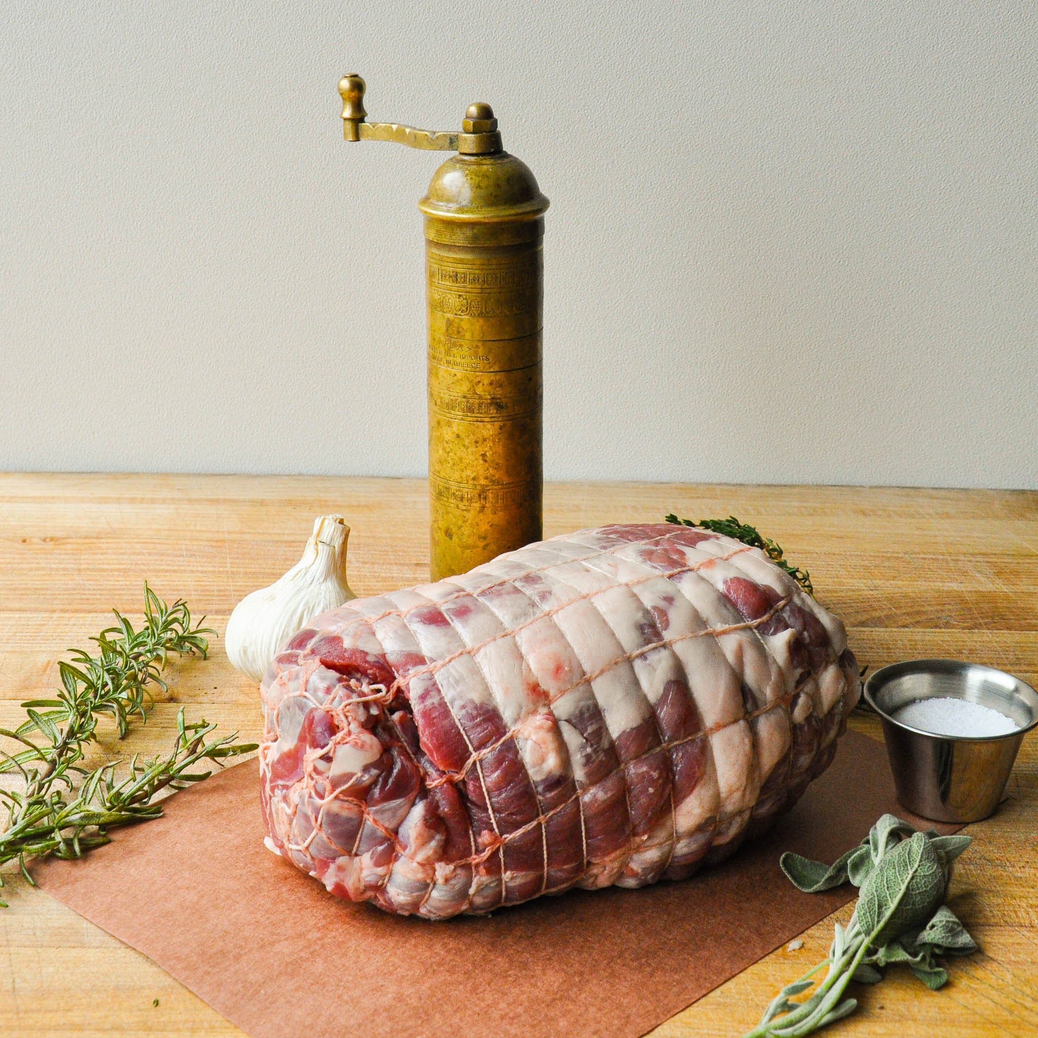 Raw meatloaf on a wooden board with herbs, garlic, and a pepper grinder.