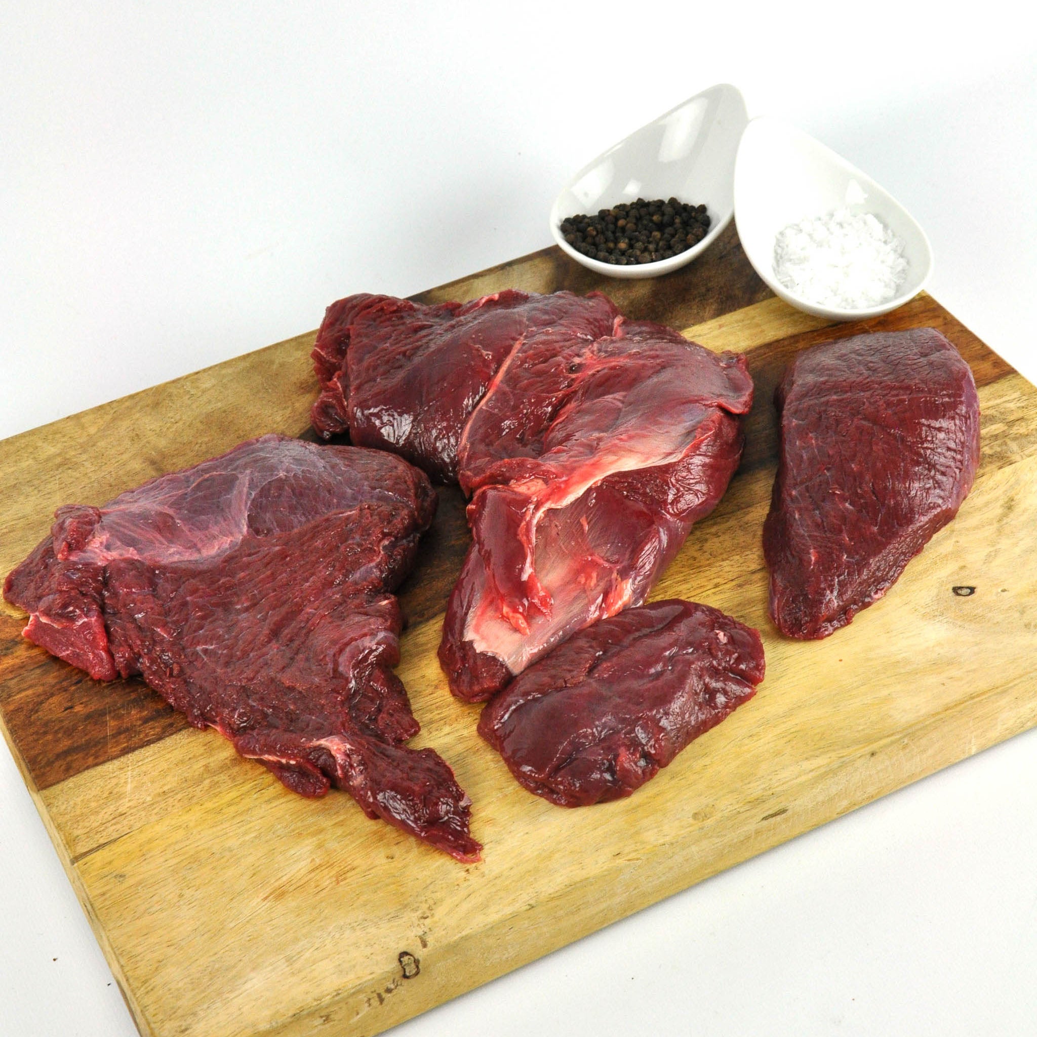 Raw beef on a wooden cutting board with salt and pepper shakers.