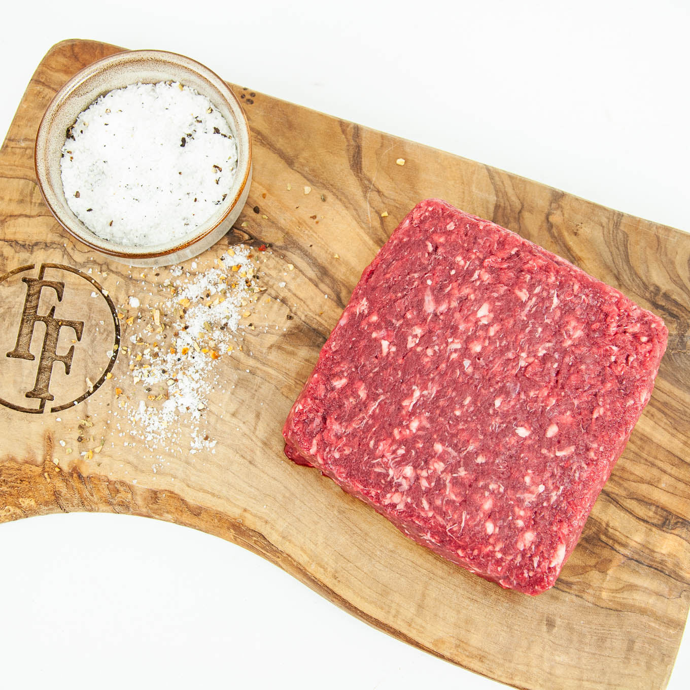 Raw ground beef on a wooden cutting board with salt and pepper shaker.
