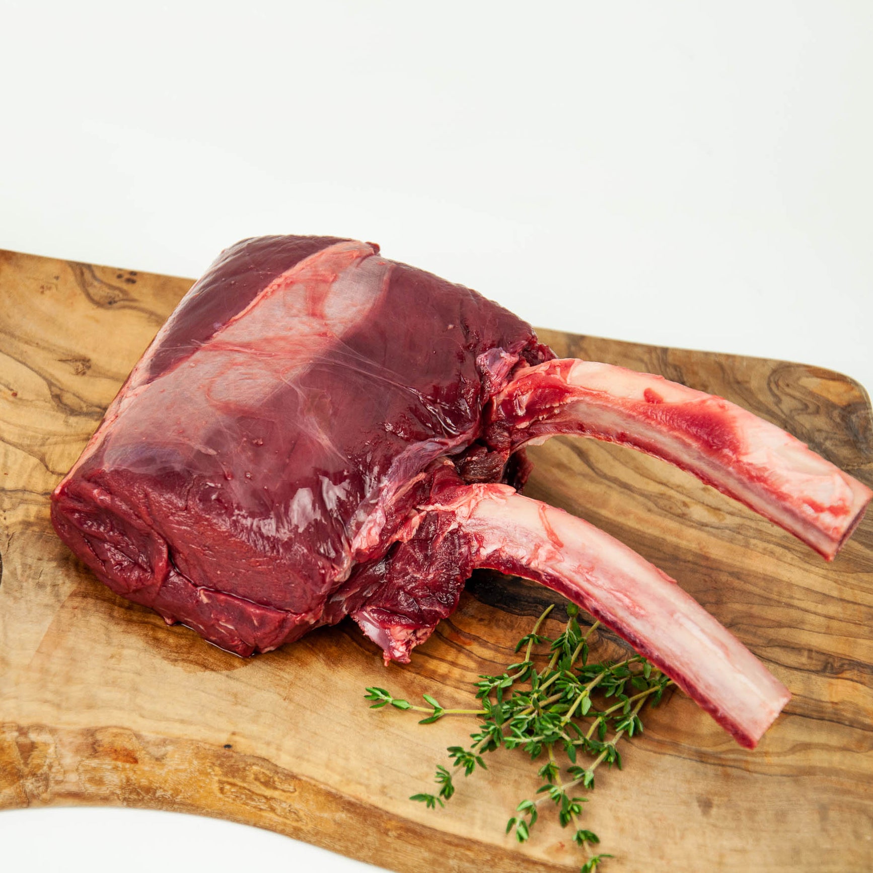Raw ribeye steak on a wooden cutting board with fresh thyme leaves.