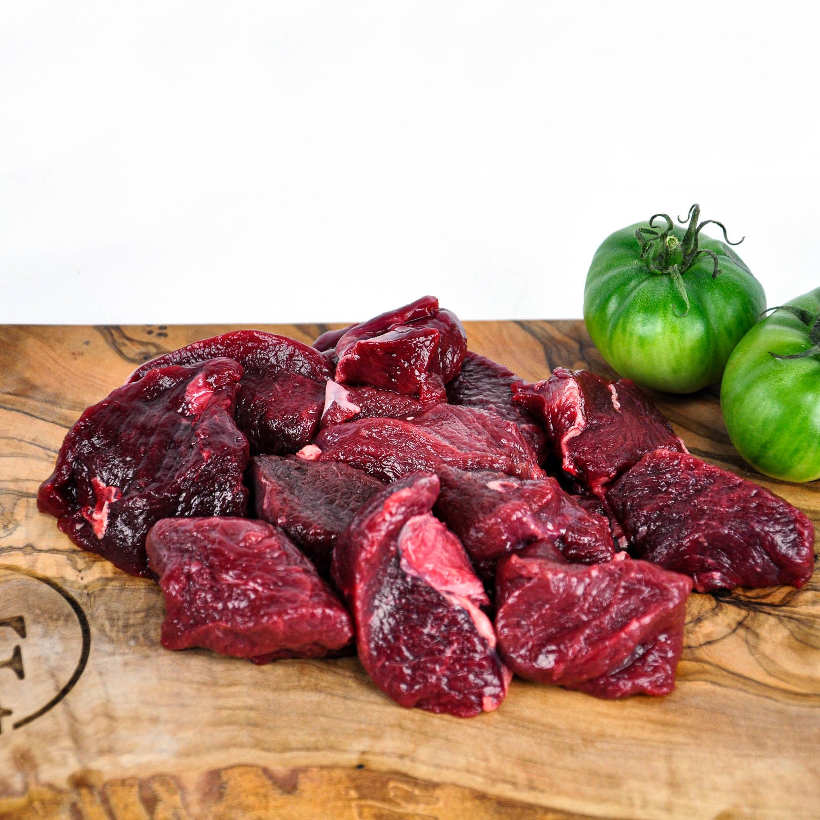 Raw venison chunks on a wooden cutting board with green tomatoes.