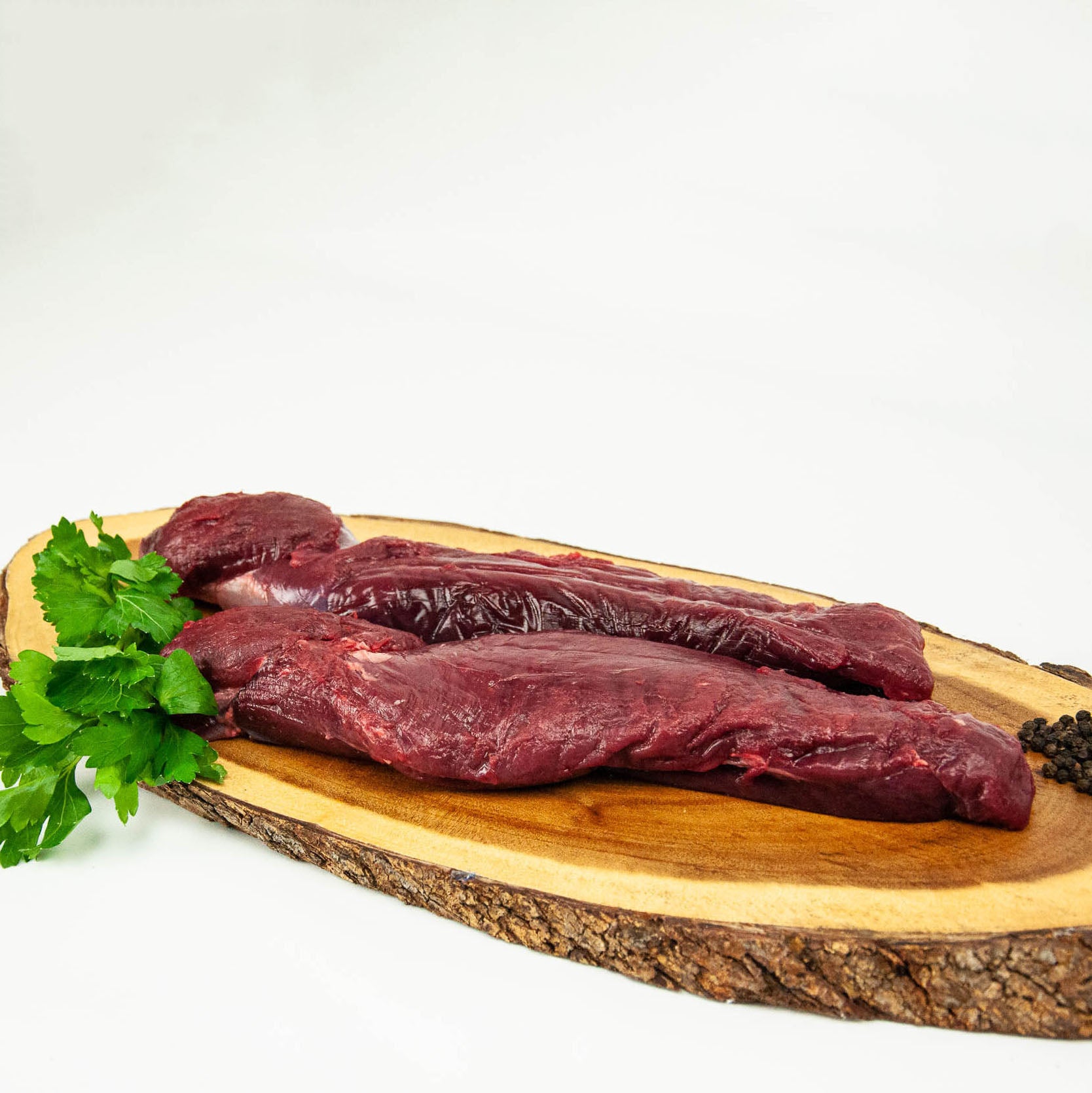 Raw beef on a wooden cutting board with parsley on a white background