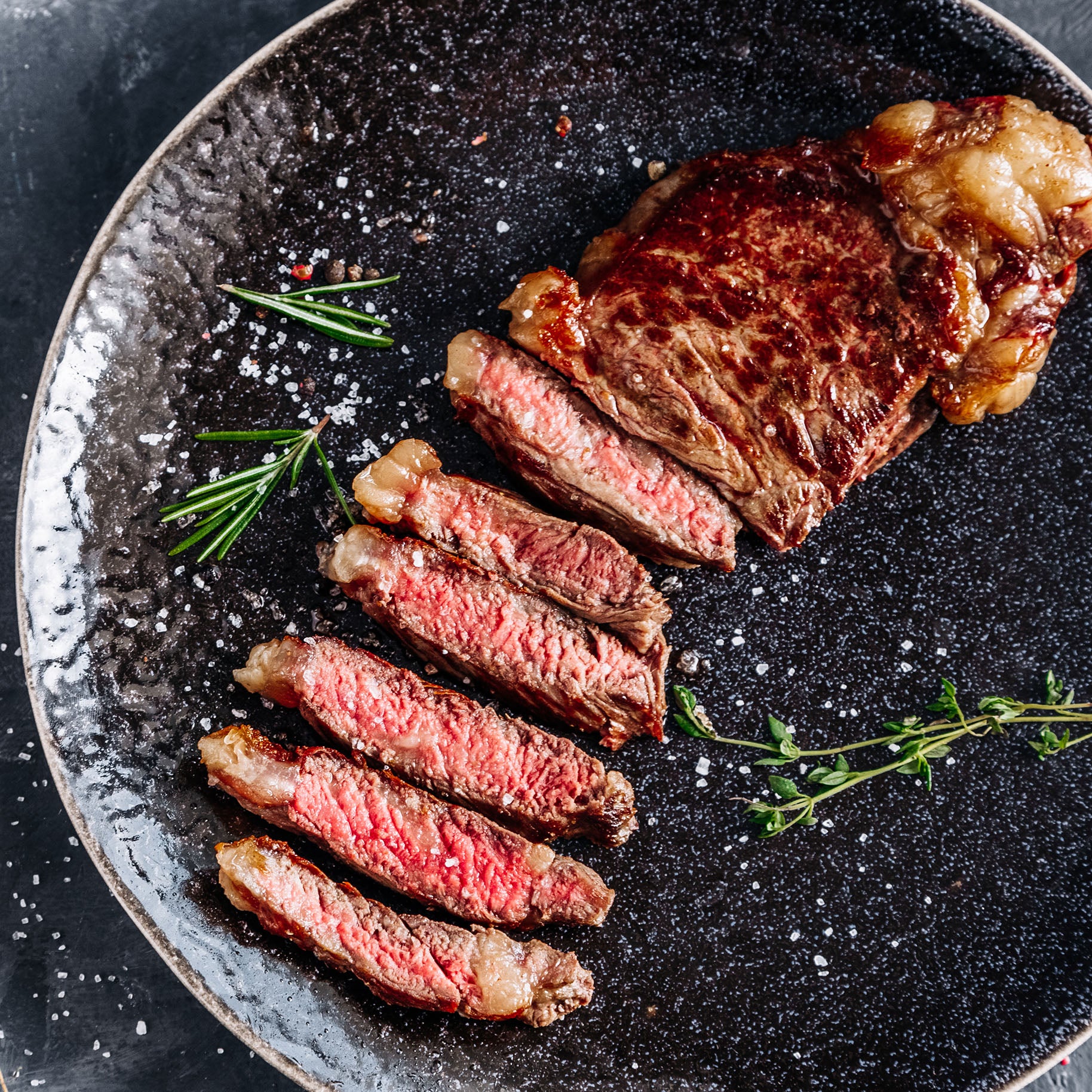 Sliced steak on a black plate with herbs