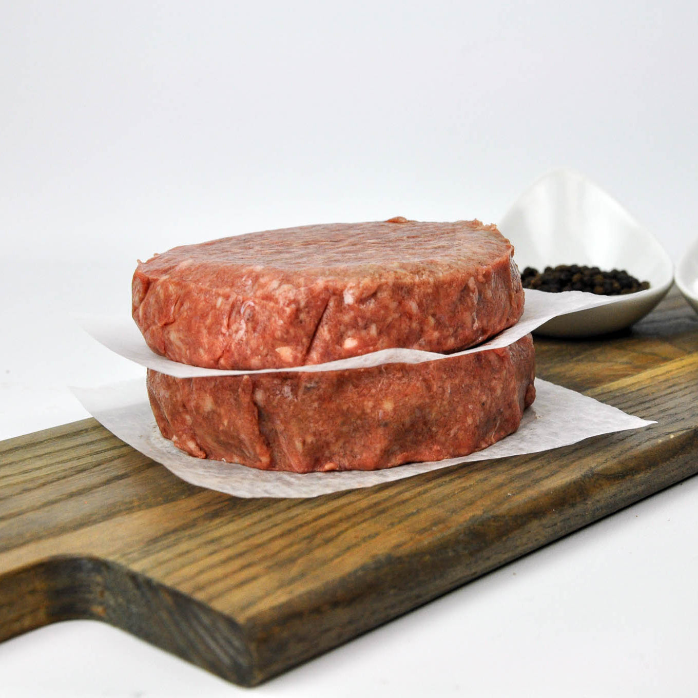 Two raw meat patties on a wooden cutting board with a white background