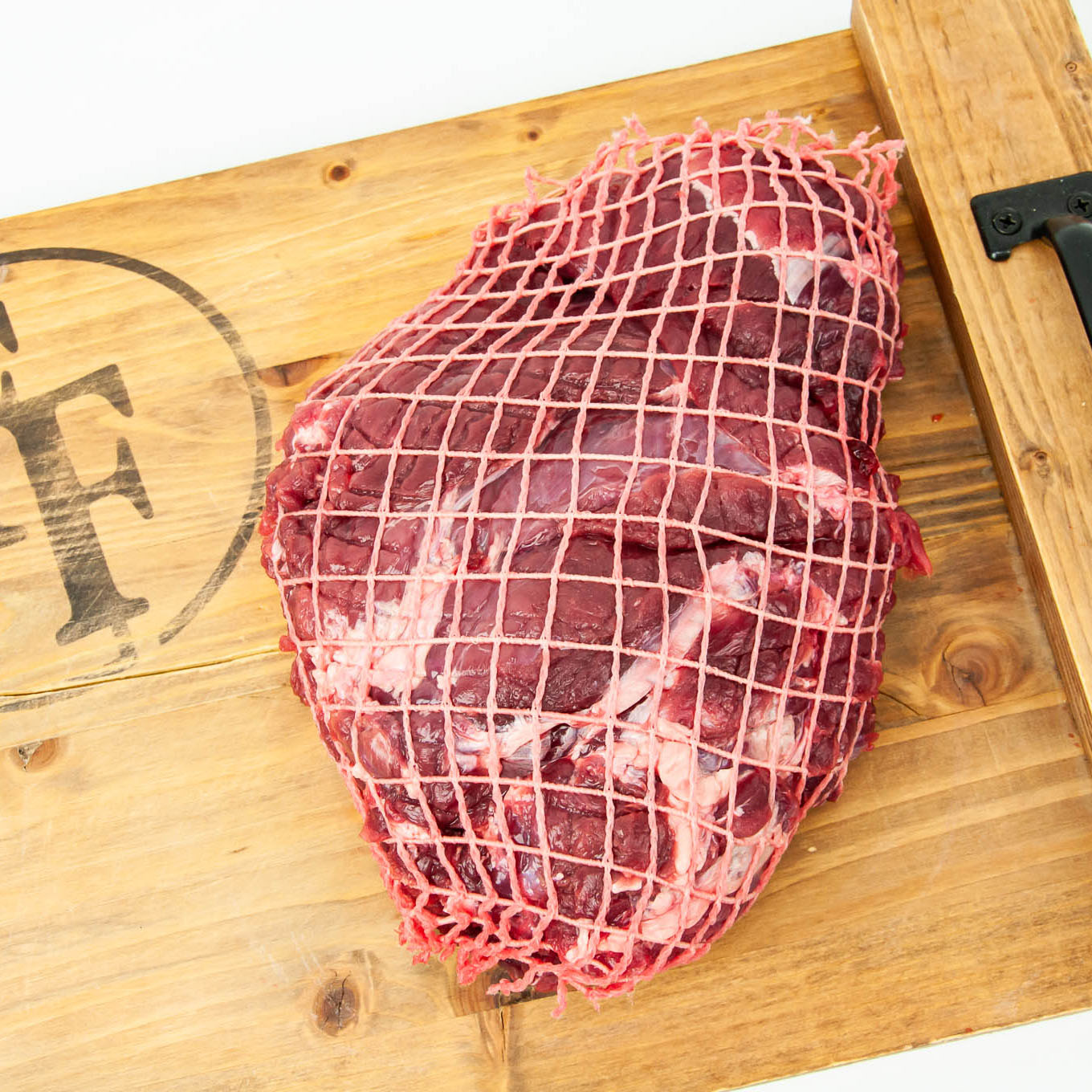 Raw meat in a net on a wooden cutting board with a brand logo.