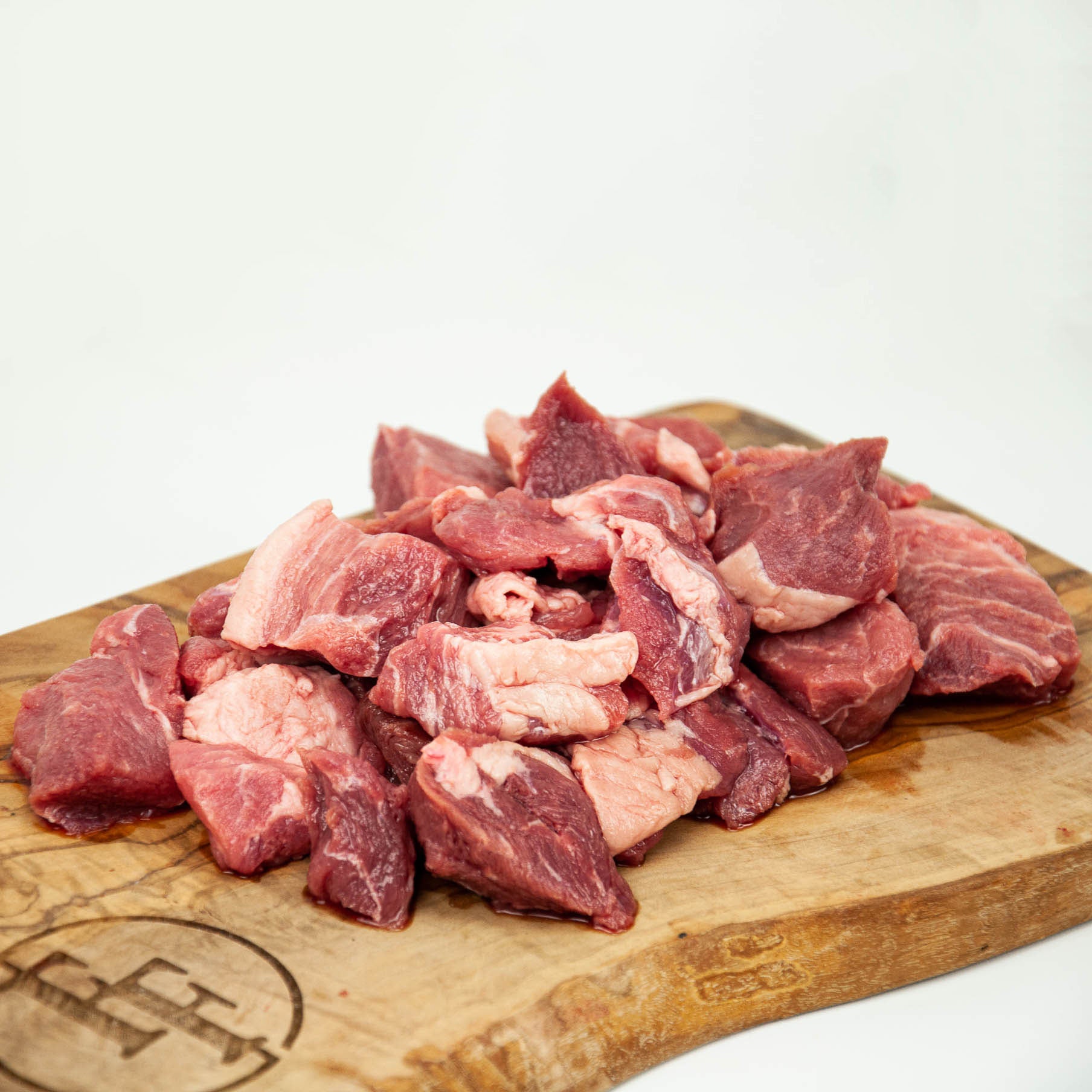 Raw beef chunks on a wooden cutting board with a white background