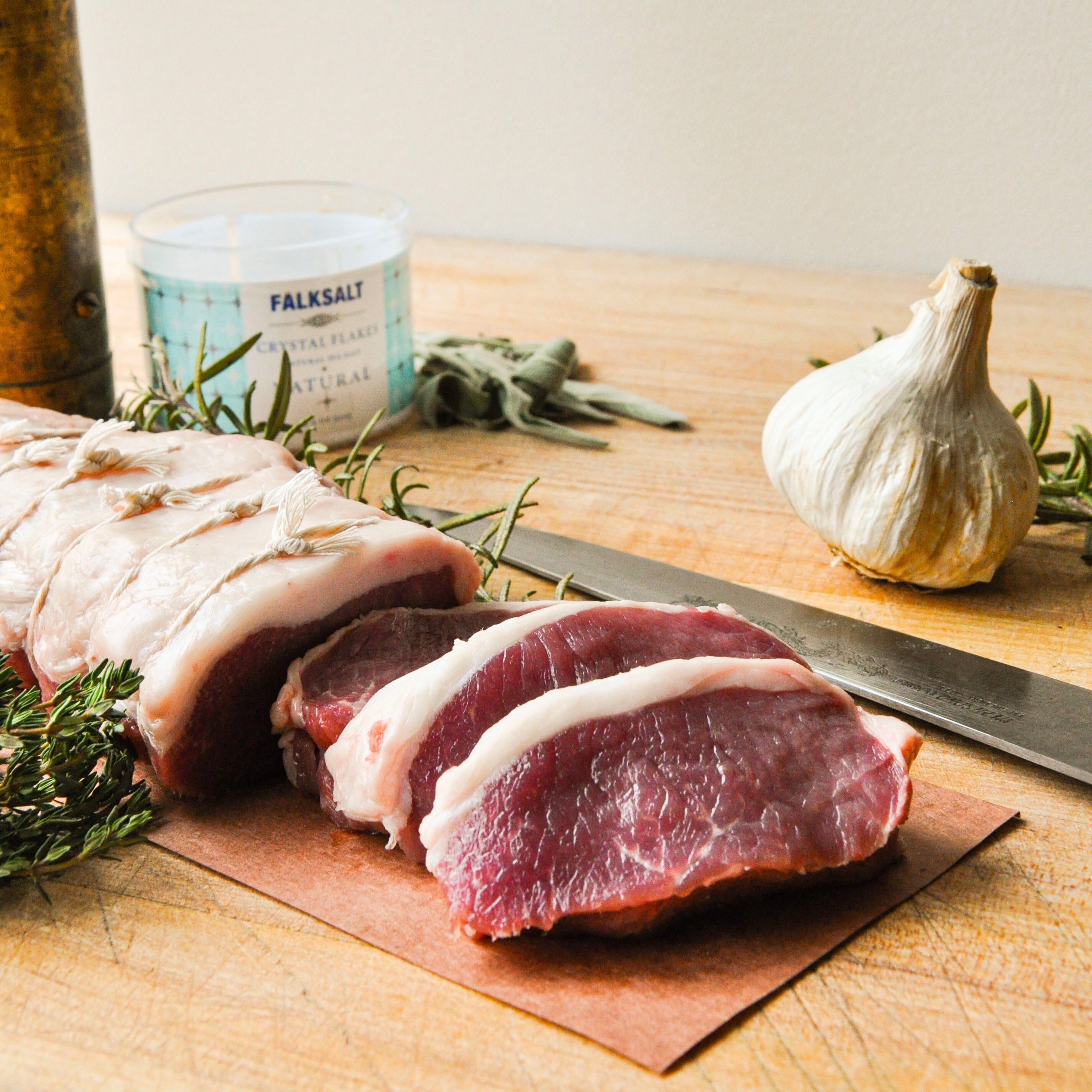 Raw meat on a wooden cutting board with herbs and a knife
