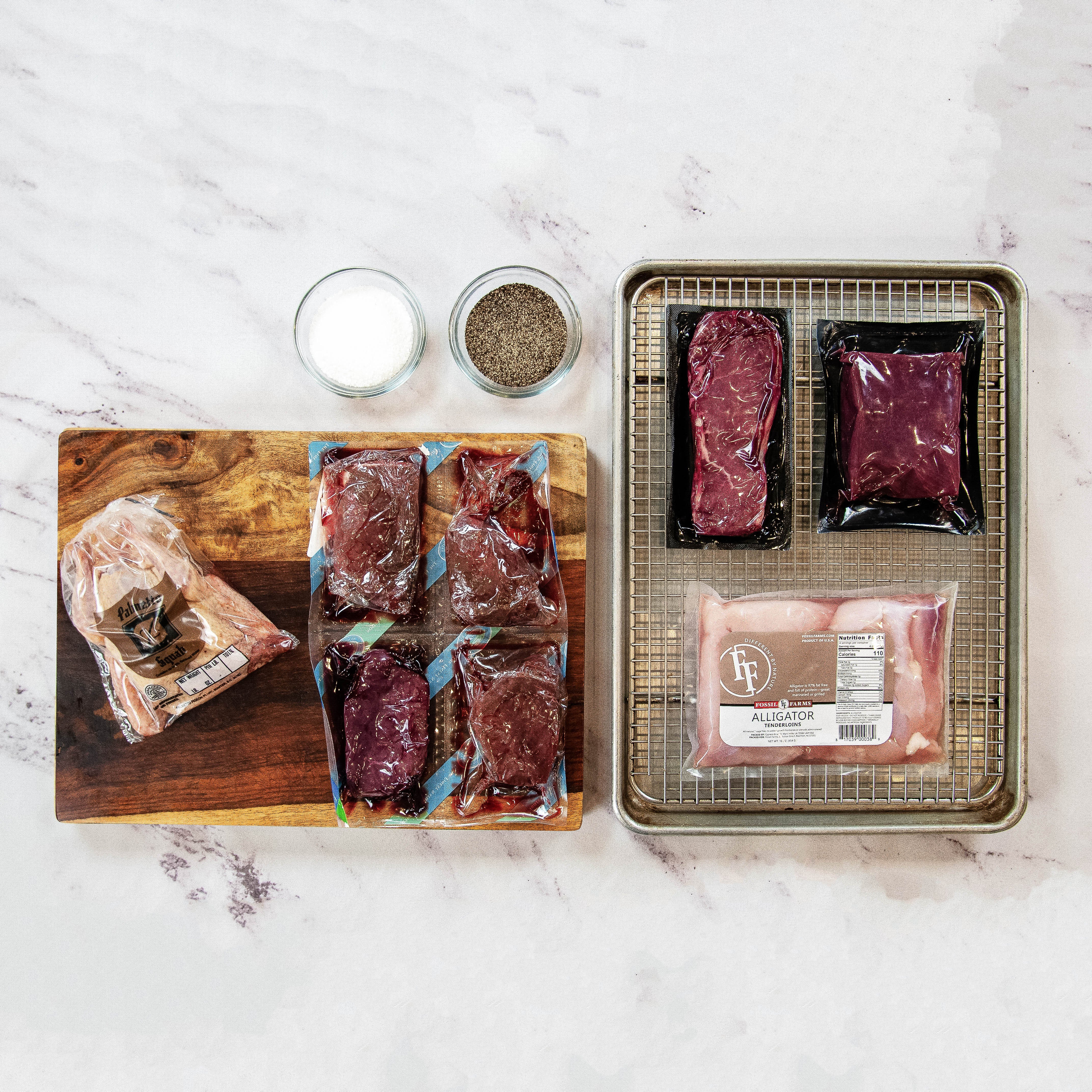 Assorted raw meat packages on a marble surface with a wooden cutting board and small containers of salt and pepper.