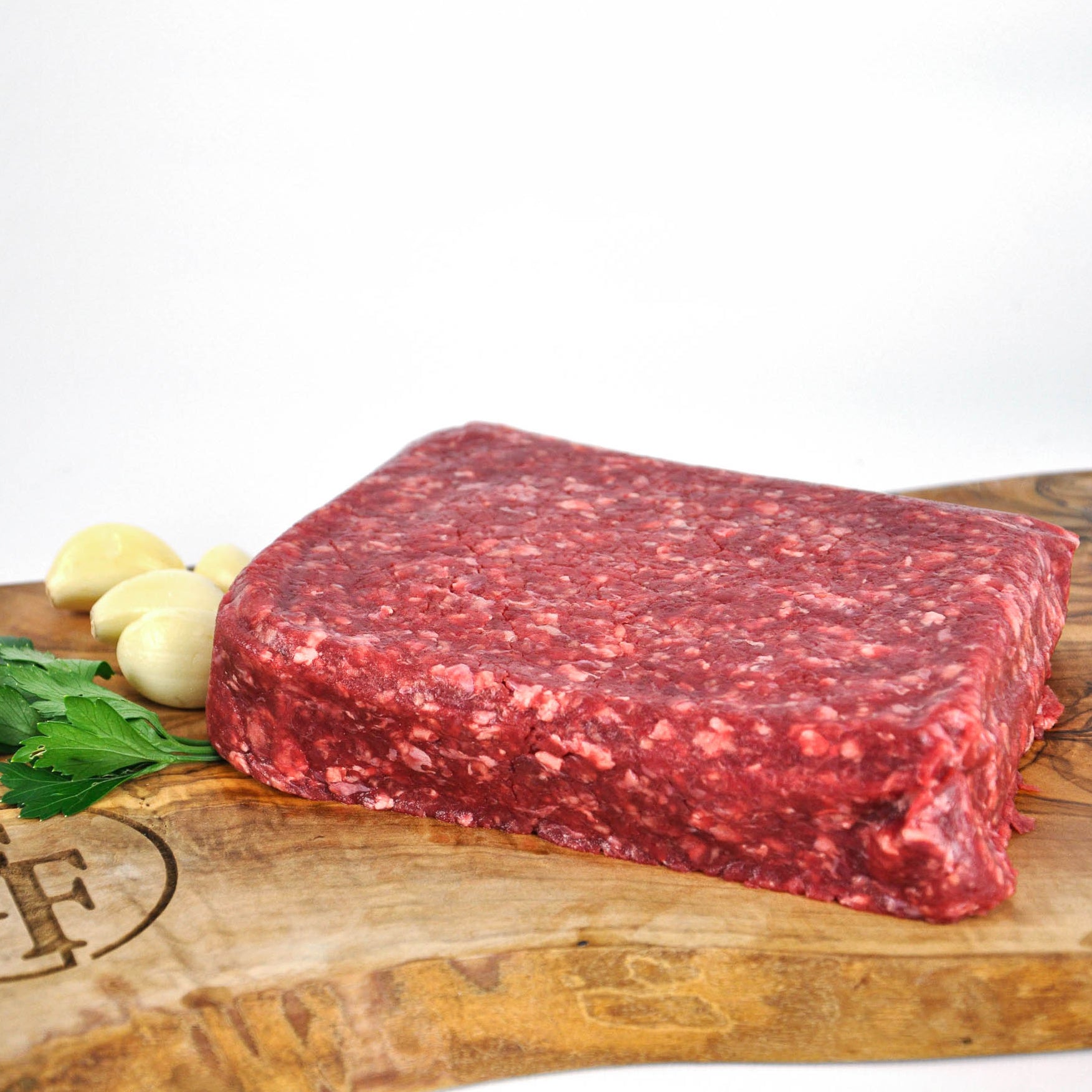 Raw ground beef on a wooden cutting board with garlic and parsley.