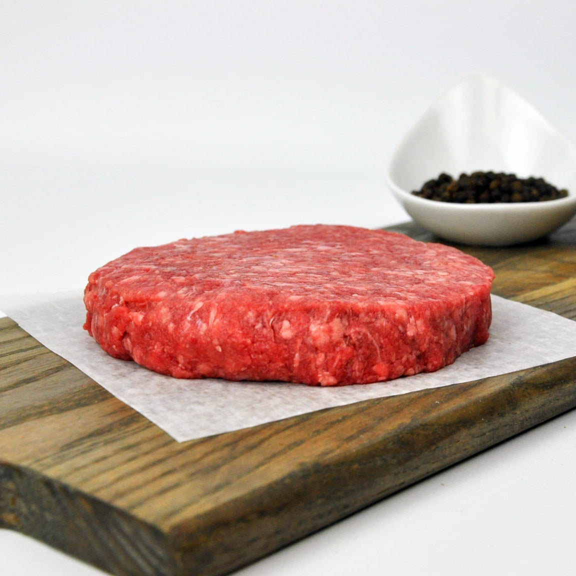 A ground Bison burger meat on a piece of parchment paper, presented on a wooden board with salt and pepper shakers in the background.