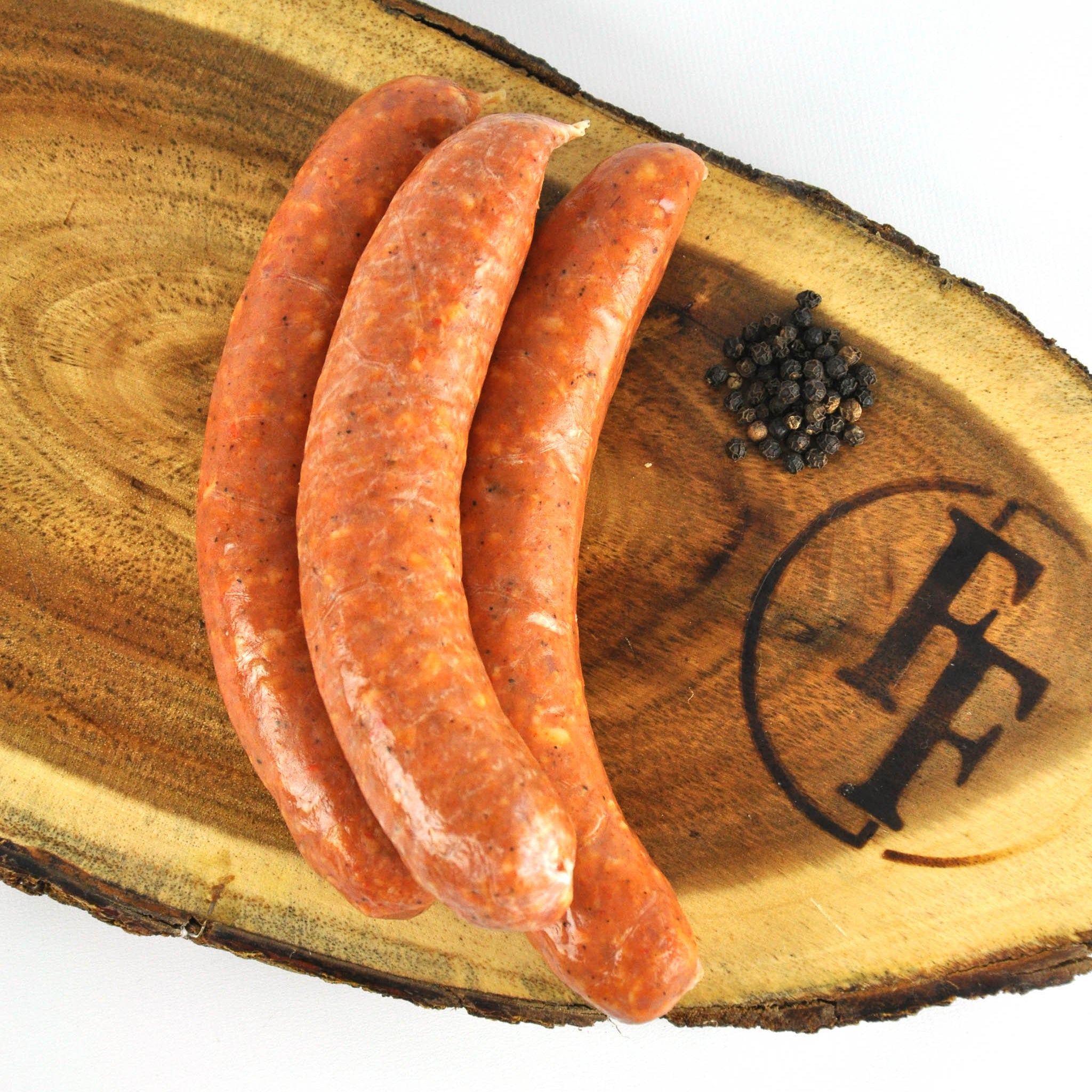 Three sausages on a wooden board with a brand logo.