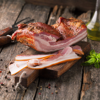 Raw bacon slices on a wooden cutting board with spices and herbs.